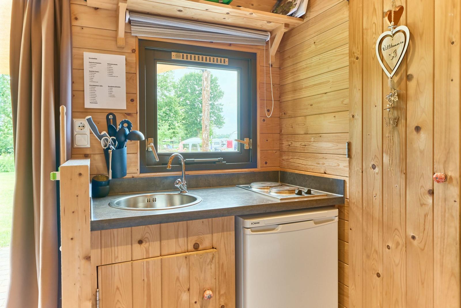 Küche mit Spüle, Herd und Kühlschrank. Holzwände und Fensterblick.