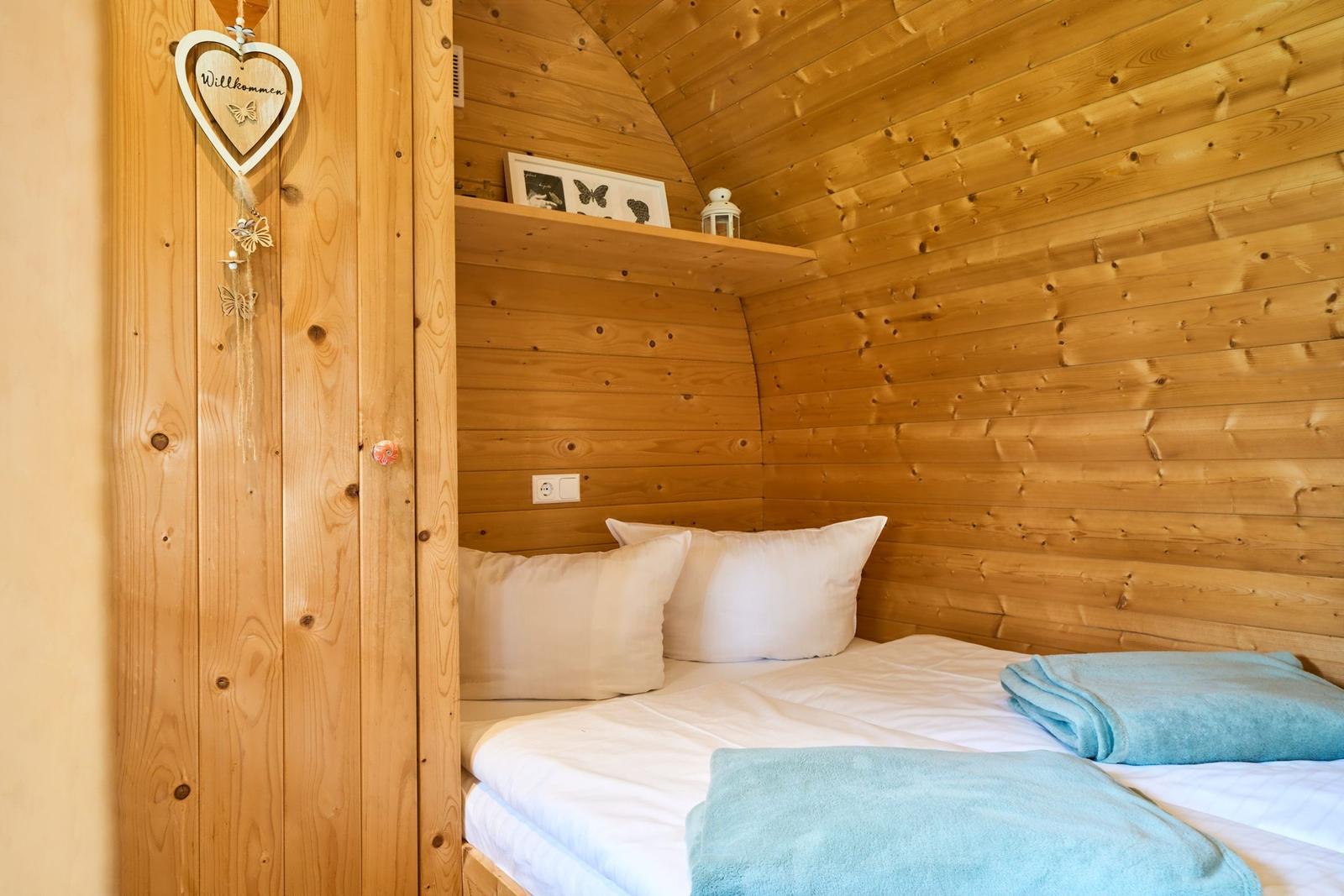Schlafzimmer mit Holzwand, Bett mit weißen Kissen und blauen Handtüchern.