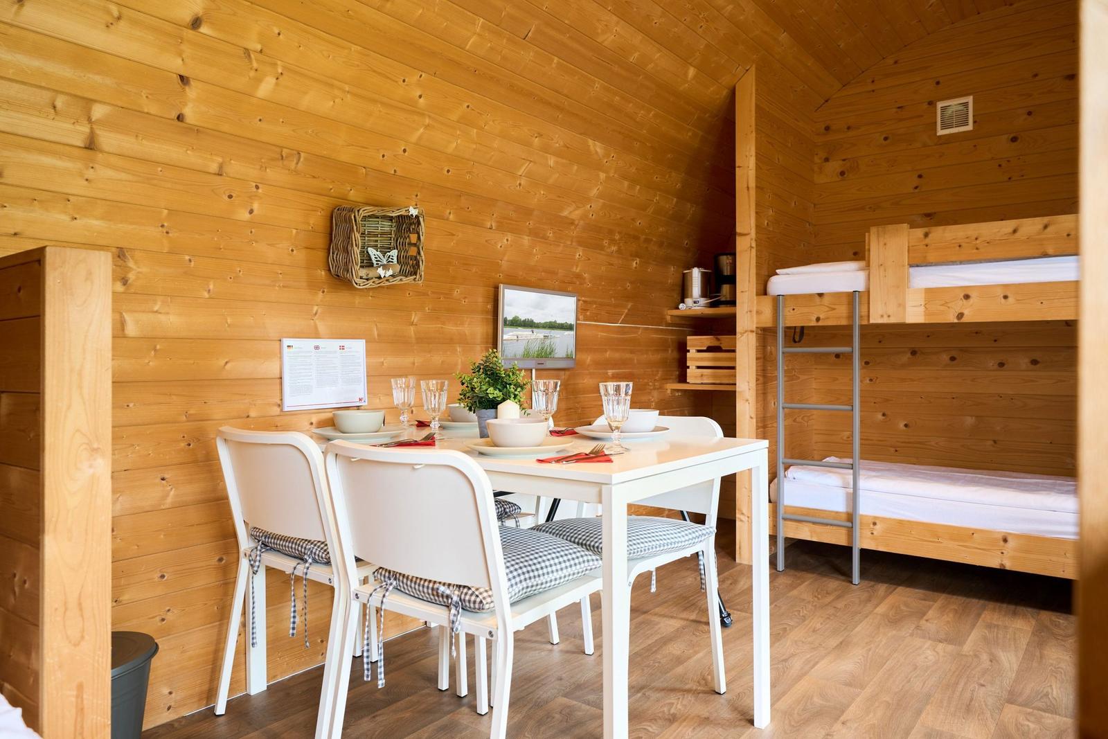 Ein Raum mit Esstisch, Stühlen und Kojenbetten an der Wand.