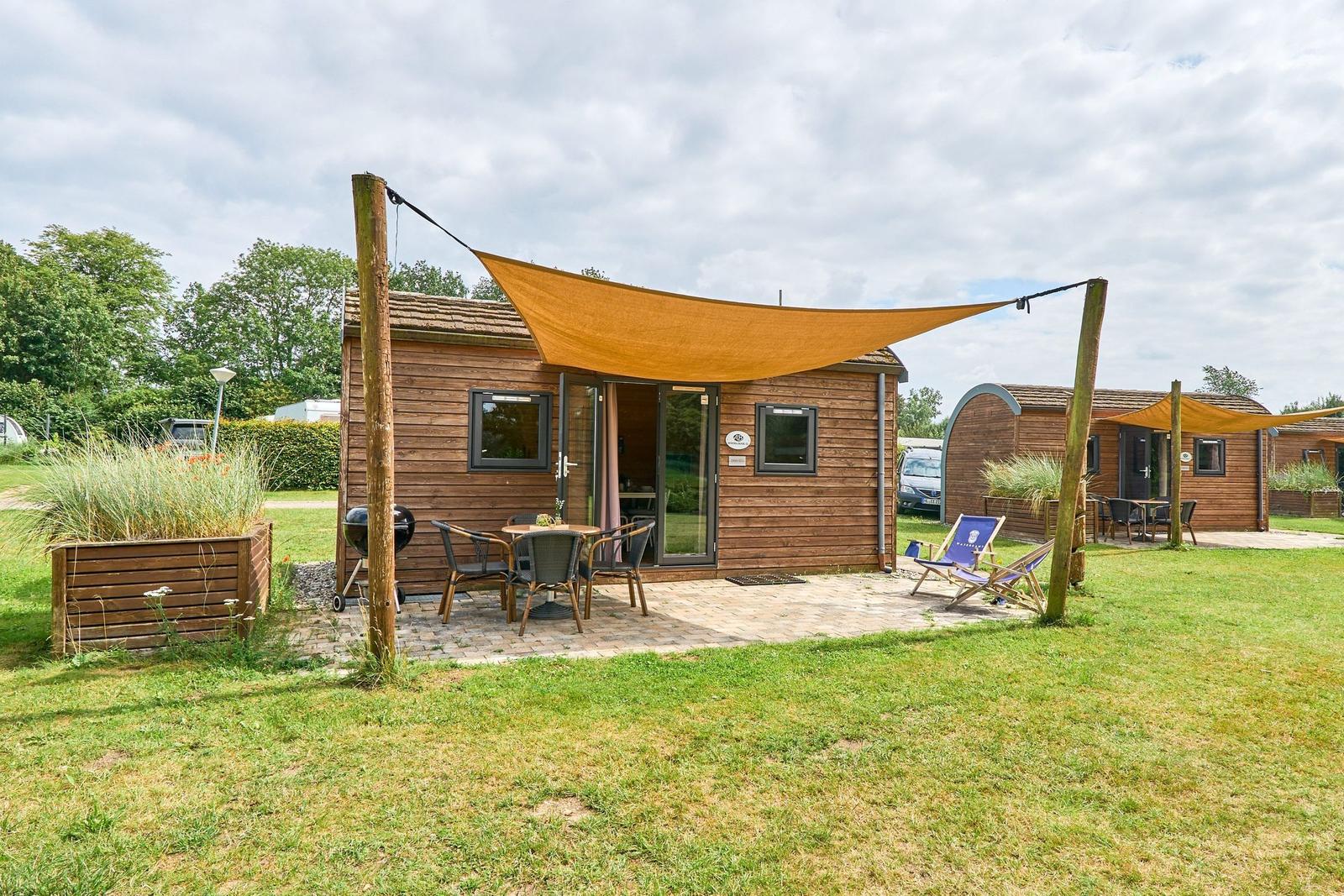 Holzhaus mit Terrasse, Sonnensegel und Gartenmöbeln.