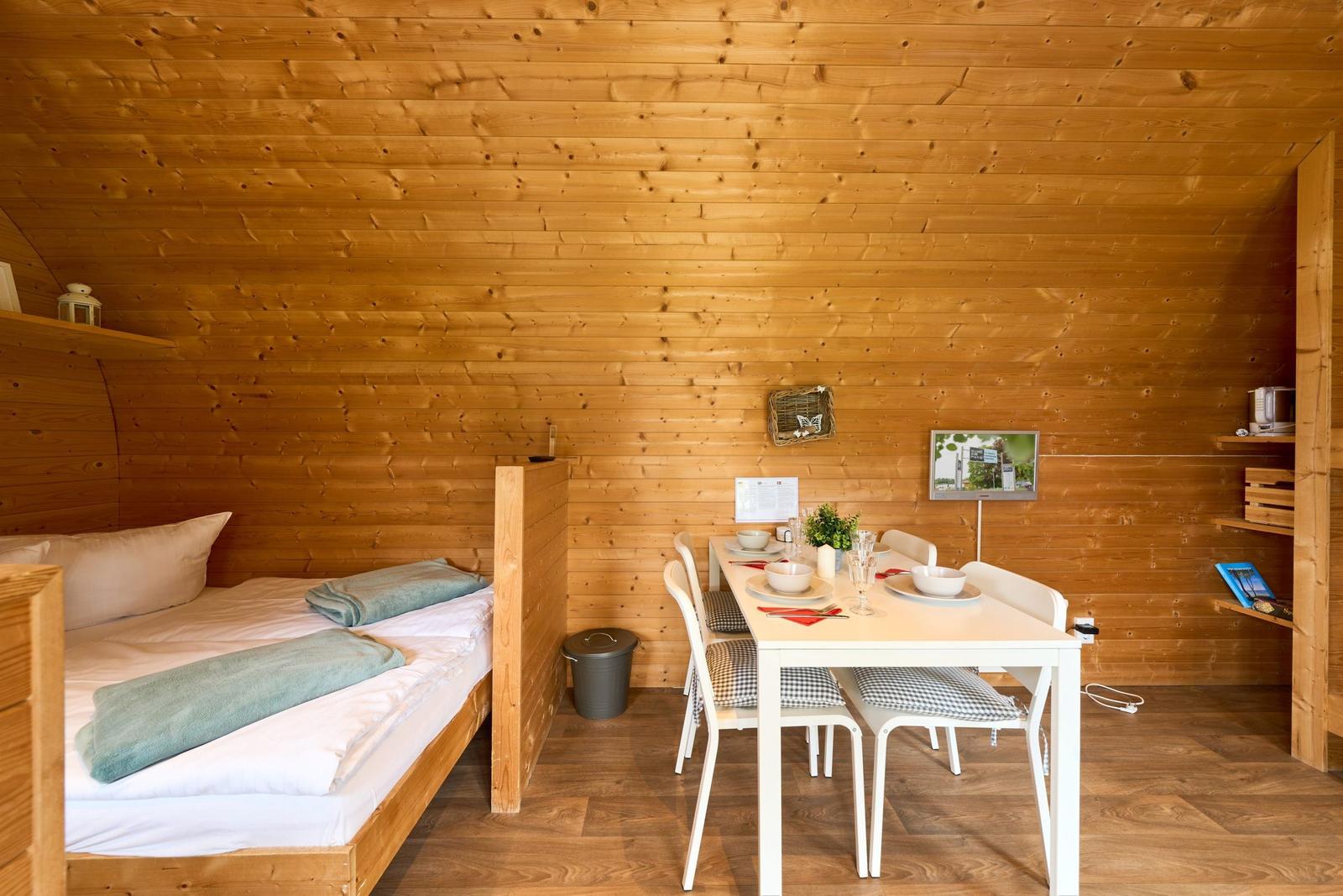 Schlafplatz mit Bett und Esstisch mit Stühlen in Holzhaus.