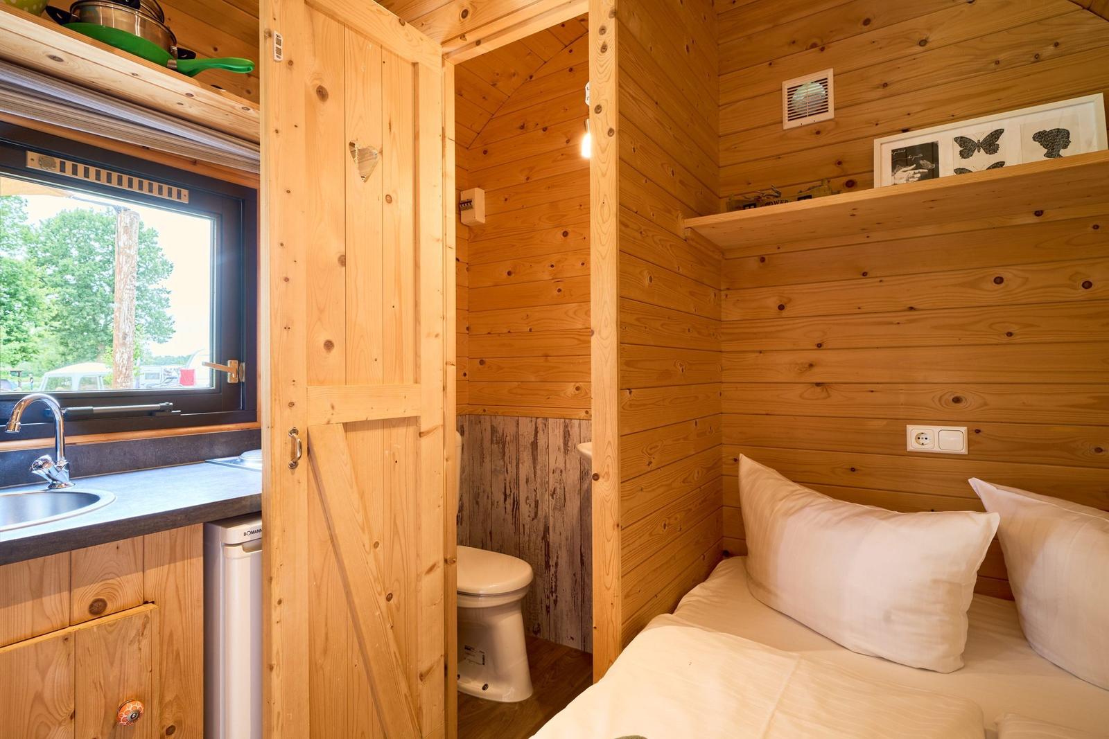 Schlafzimmer mit Bett, Küchenzeile und Toilette in Holzhaus.