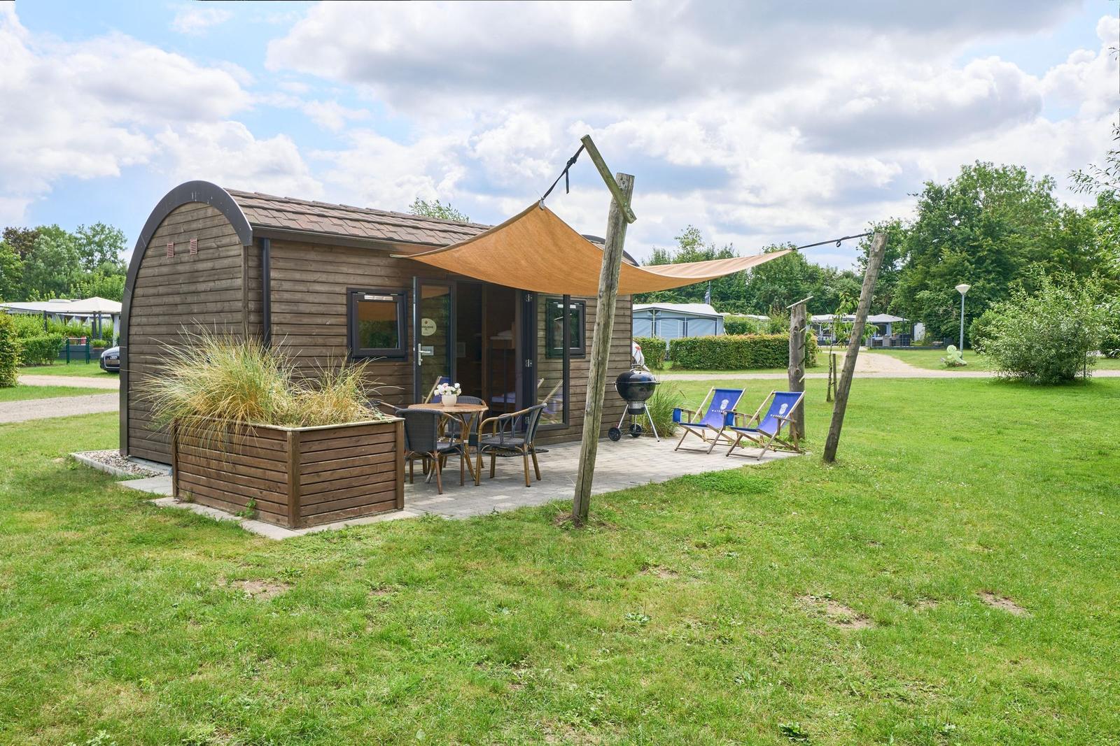 Holzhaus mit Terrasse, Sonnensegel, Grill und Liegestühle im Grün.