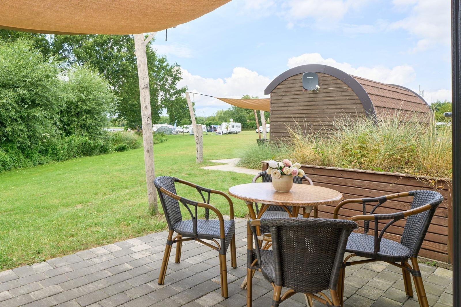 Terrasse mit Tisch und Stühlen unter Markise. Im Hintergrund Grasfläche und Holzhaus.