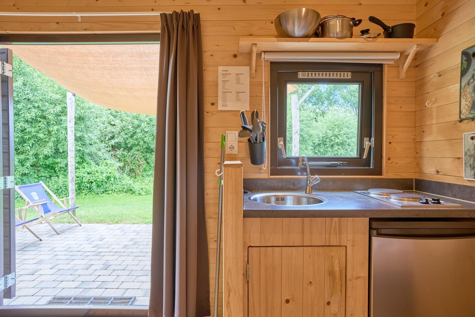 Küche mit Spüle, Herd und Kühlschrank. Draußen liegt ein Terrassenbereich mit Stuhl.