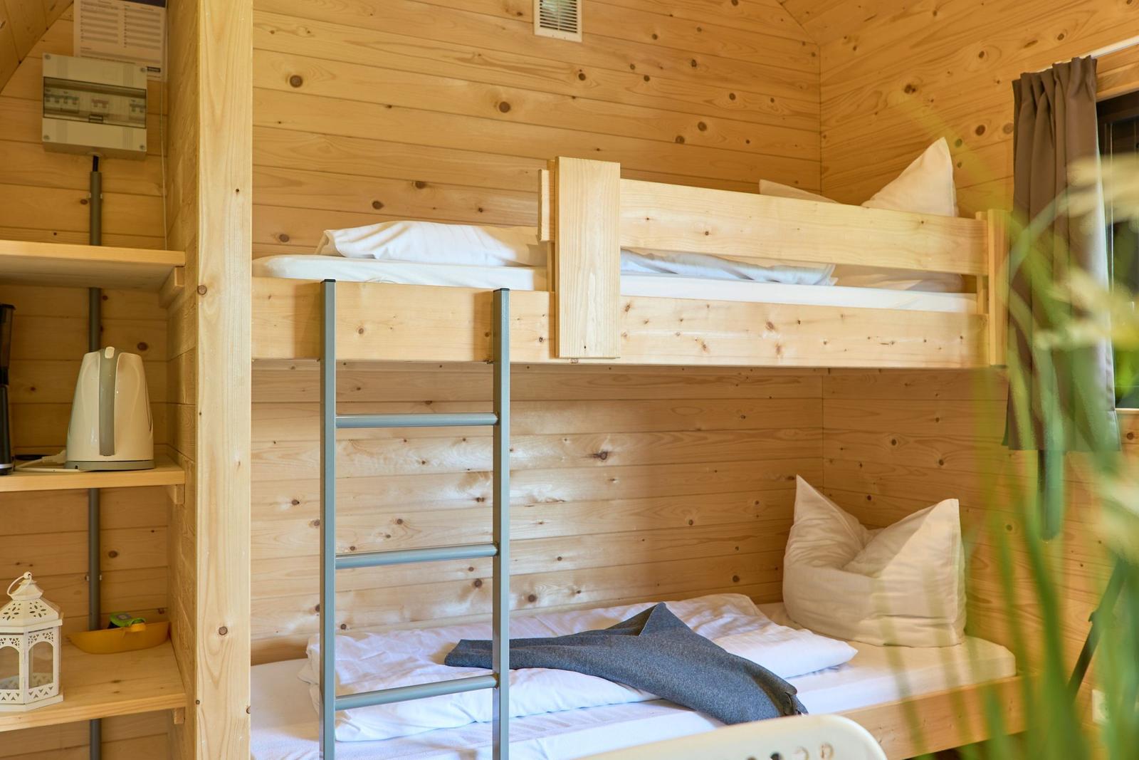 Hochbetten mit Matratzen und Kissen in Holzhaus. Metallleiter und Regal mit Kaffeemaschine.