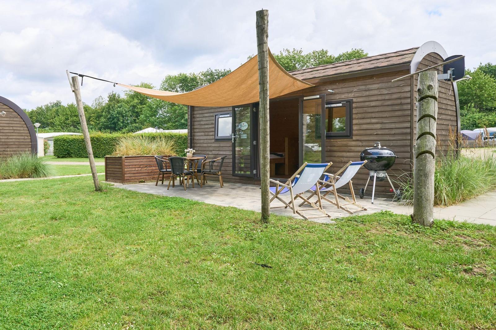 Holzhütte mit Terrasse, Sonnensegel, Liegestühlen und Grill.