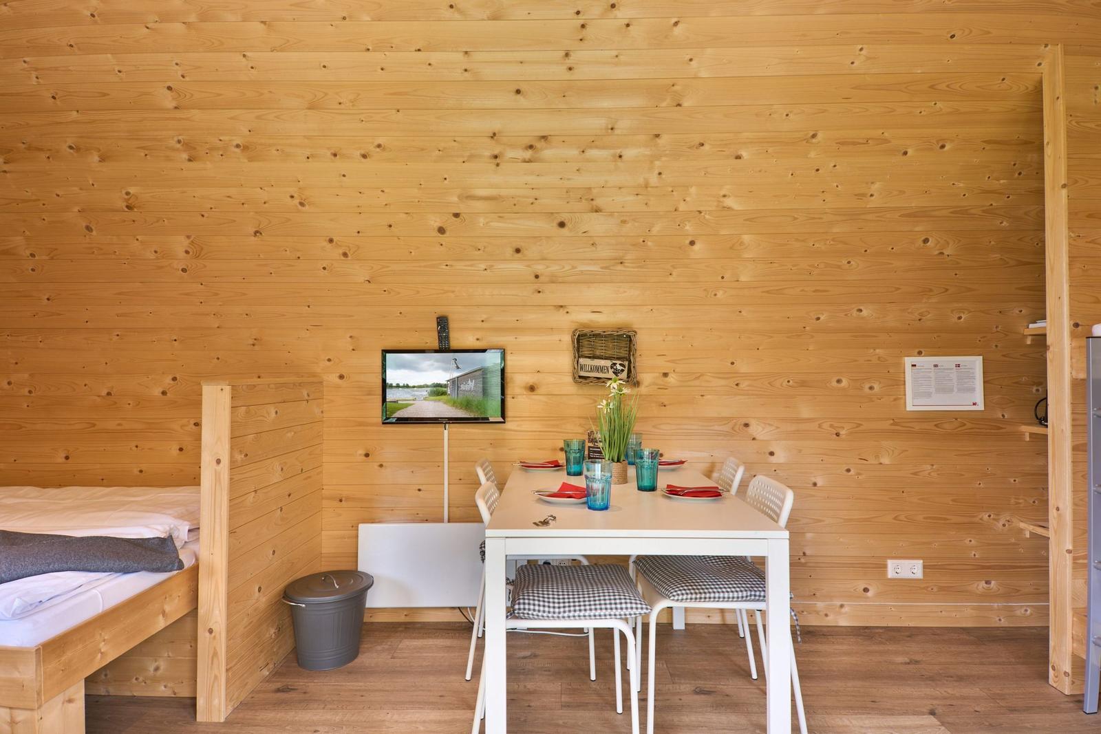 Ein Raum mit Holzwand, Tisch, Stühlen, Bett und Fernseher.