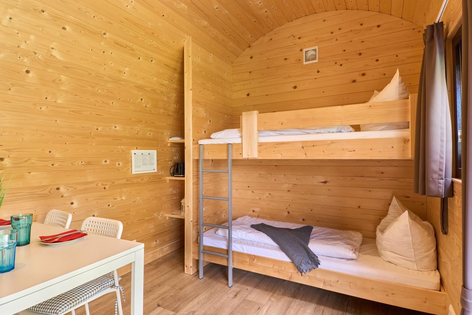 Zimmer mit Doppelstockbett, Esstisch und Holzwand.