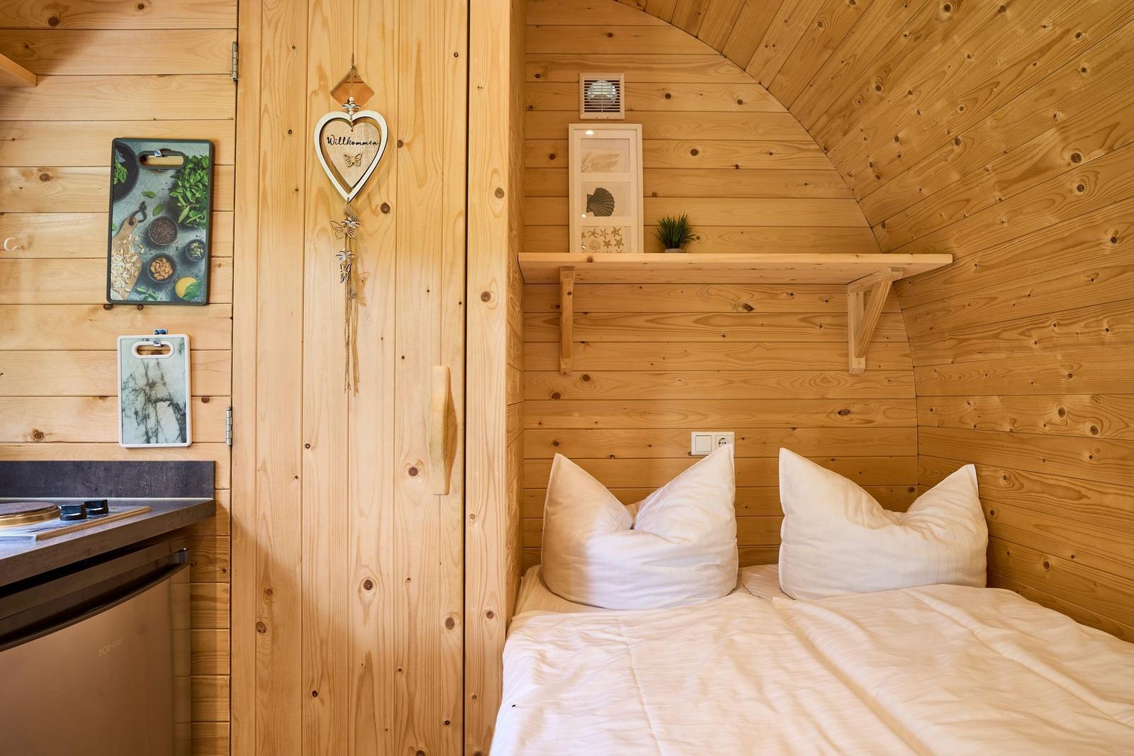 Schlafzimmer mit Bett, Holzwand und Küchenzeile.