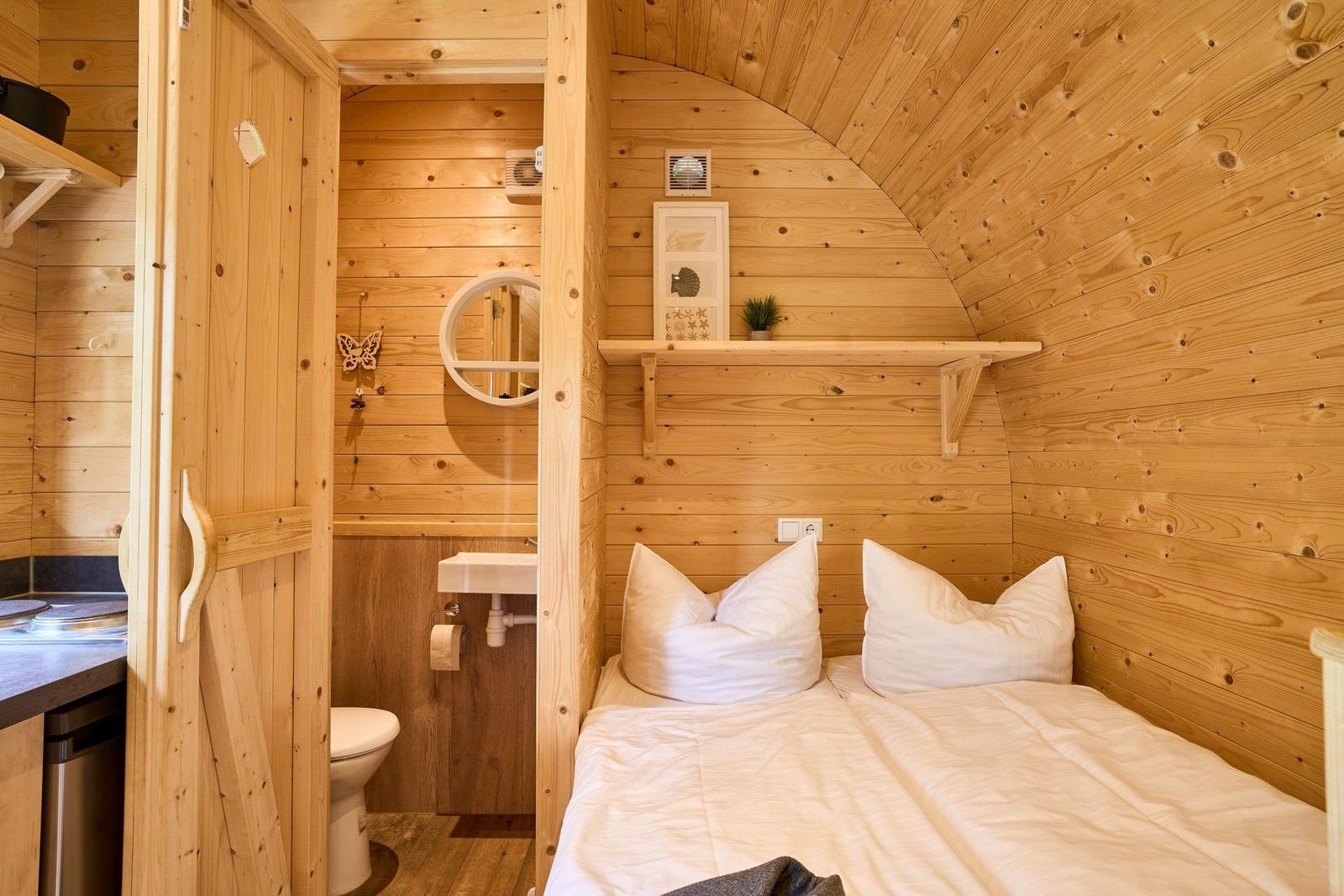 Schlafzimmer mit Holzwand und Bett. Nebenraum mit Toilette und Waschbecken.