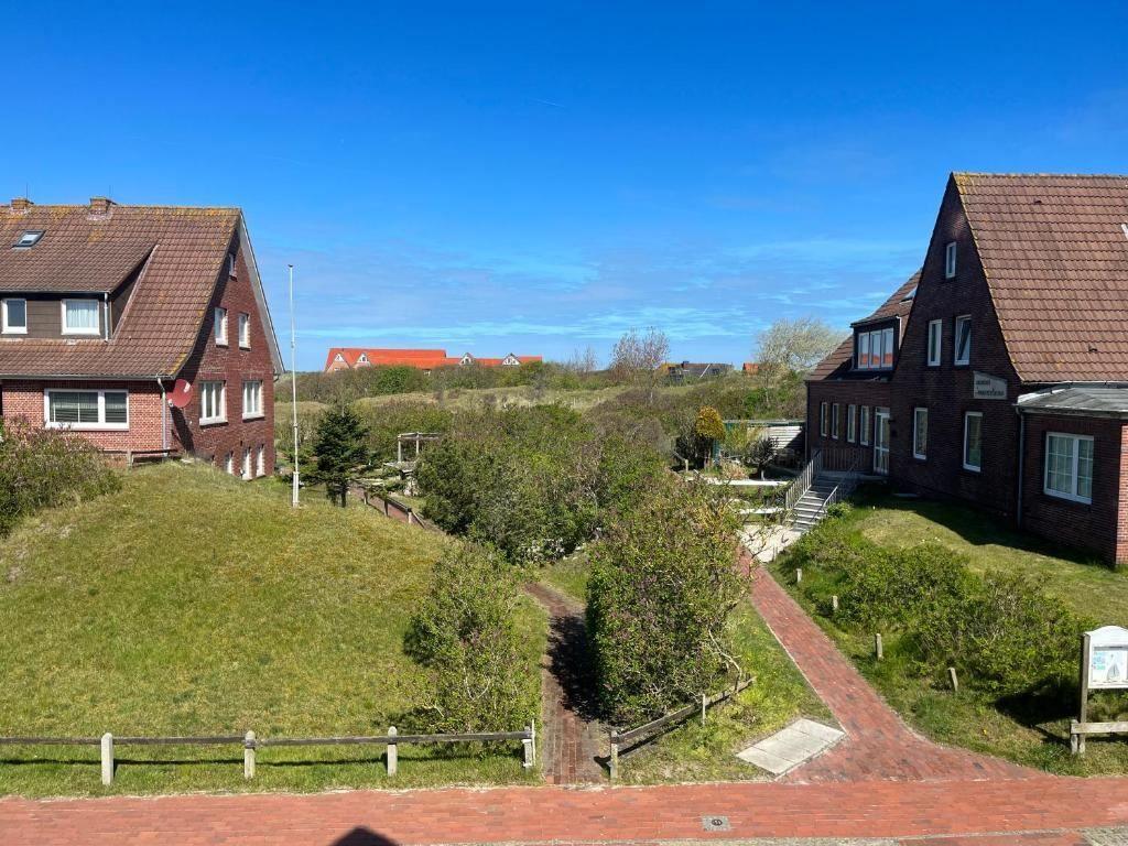 Zwei Häuser mit rotem Dach und grünem Grundstück unter blauem Himmel.