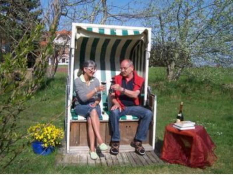 Ein Paar sitzt in einem Strandkorb auf einer Terrasse mit Tisch, Blumen und Flasche.