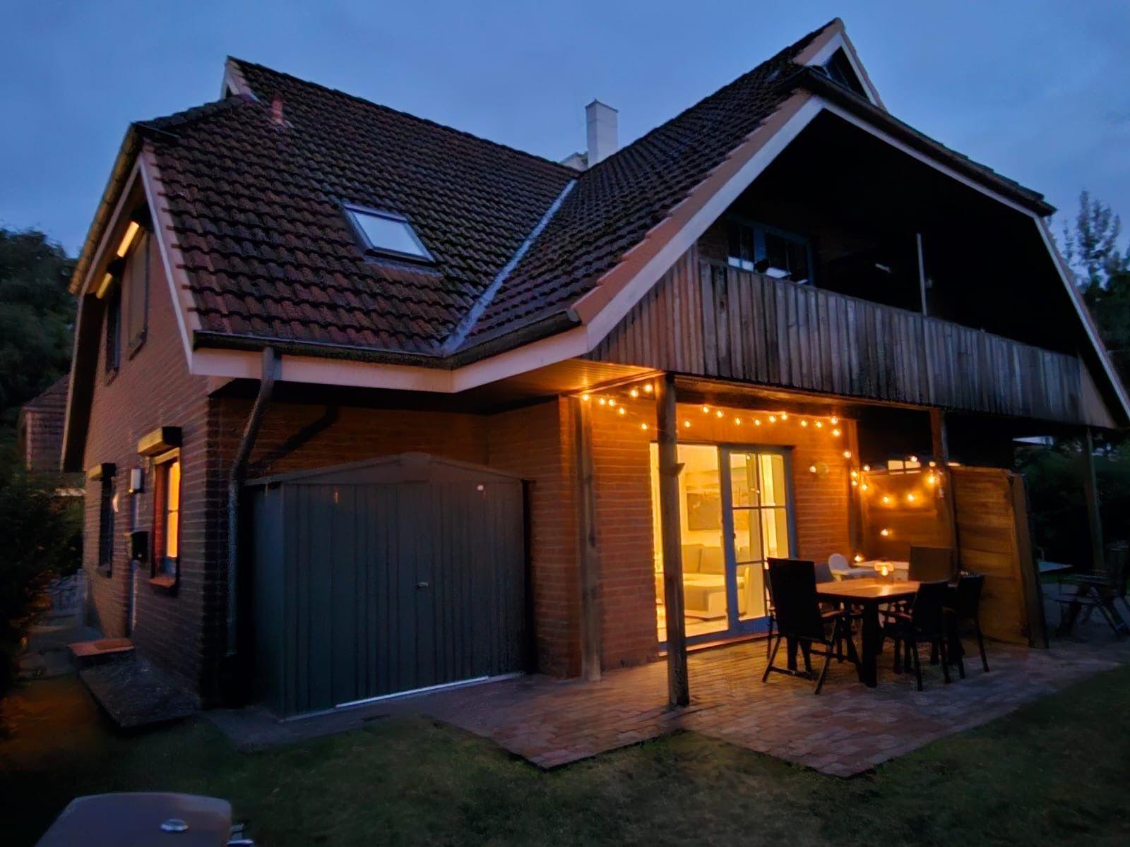Haus mit Terrasse, Tisch, Stühlen und Lichterkette bei Dämmerung.