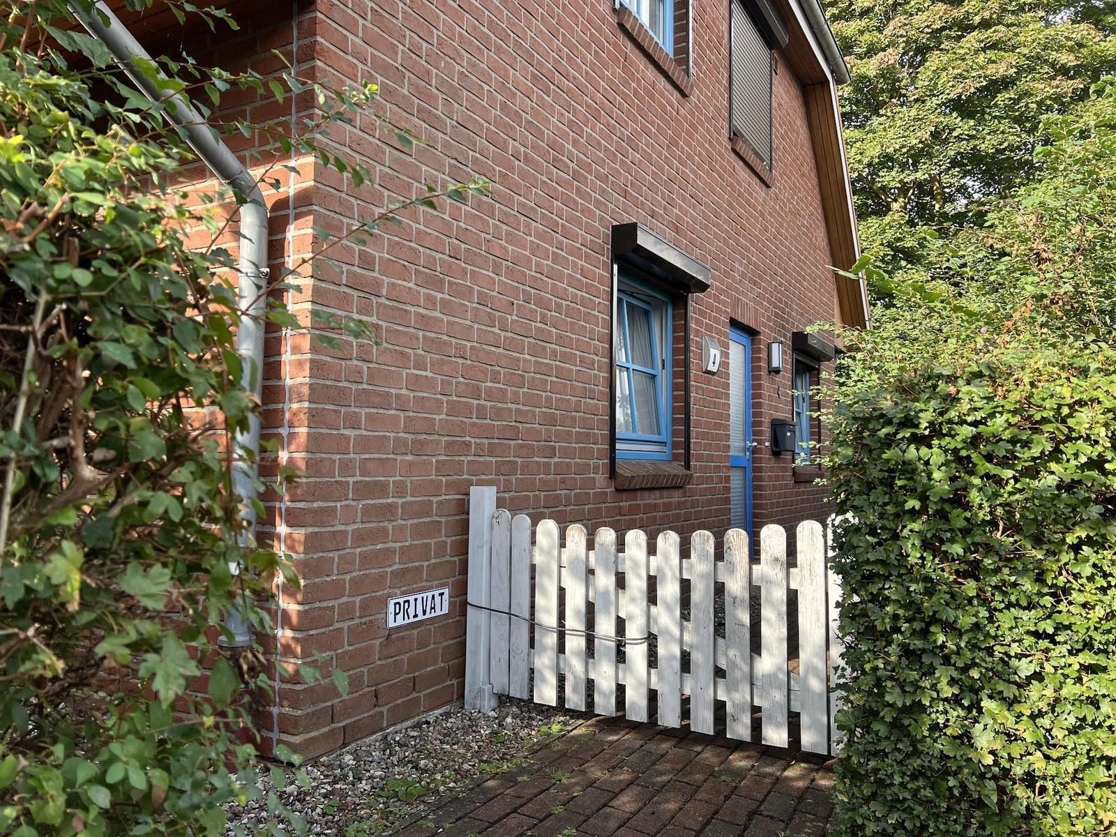 Rotes Backsteinhaus mit blauen Fenstern und weißem Zaun. Privatgeheimniszeichen angebracht.