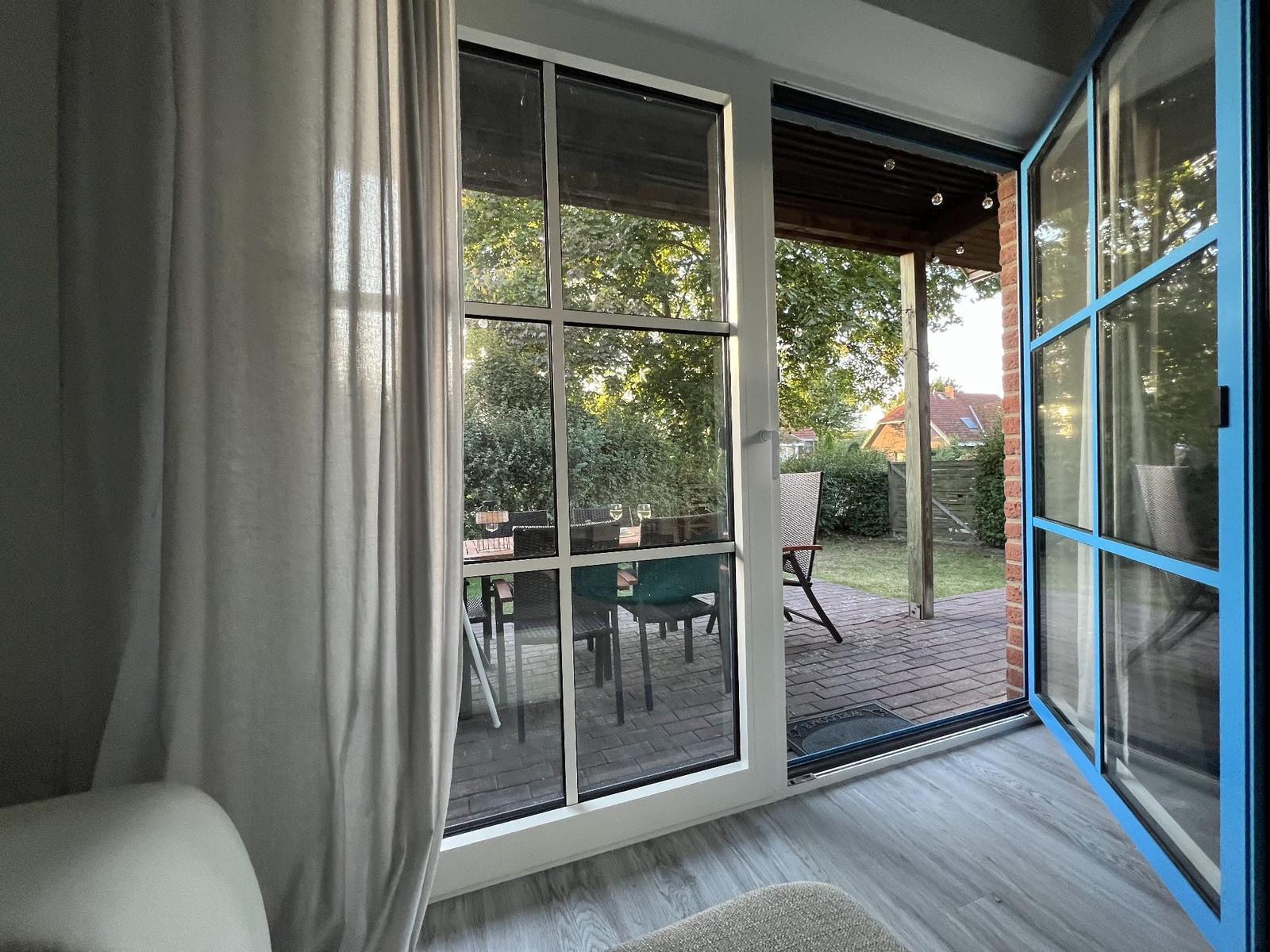 Durch die Glastüren ist der Garten mit Tisch und Stühlen zu sehen.