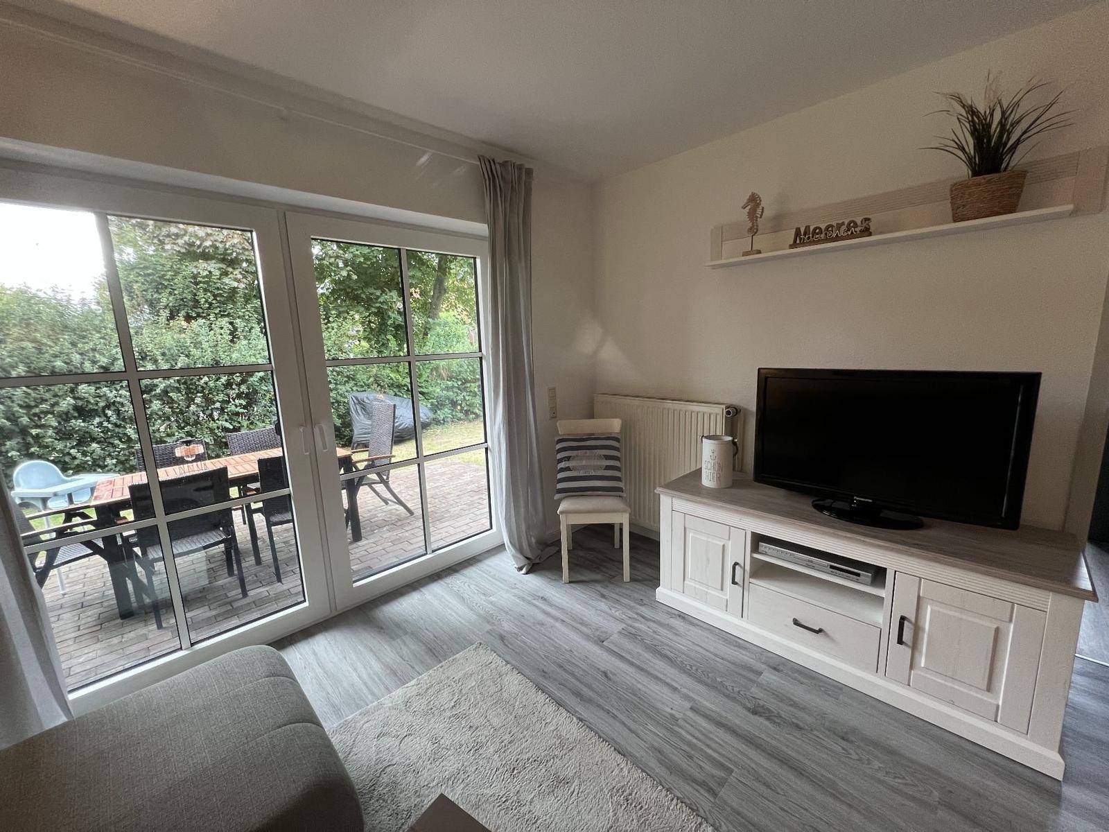Wohnzimmer mit TV-Schrank, Terrasse und Gartenansicht.