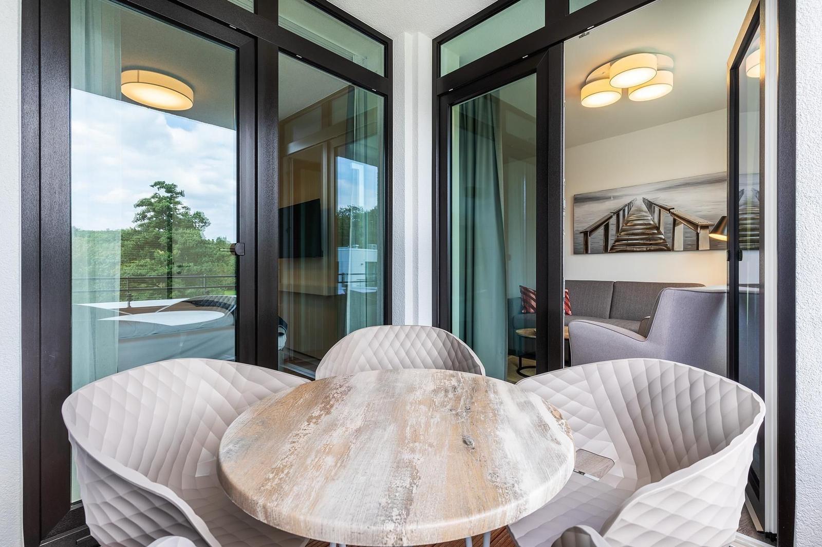 Terrasse mit runden Tisch und weißen Stühlen. Blick in Wohnzimmer und Schlafzimmer.