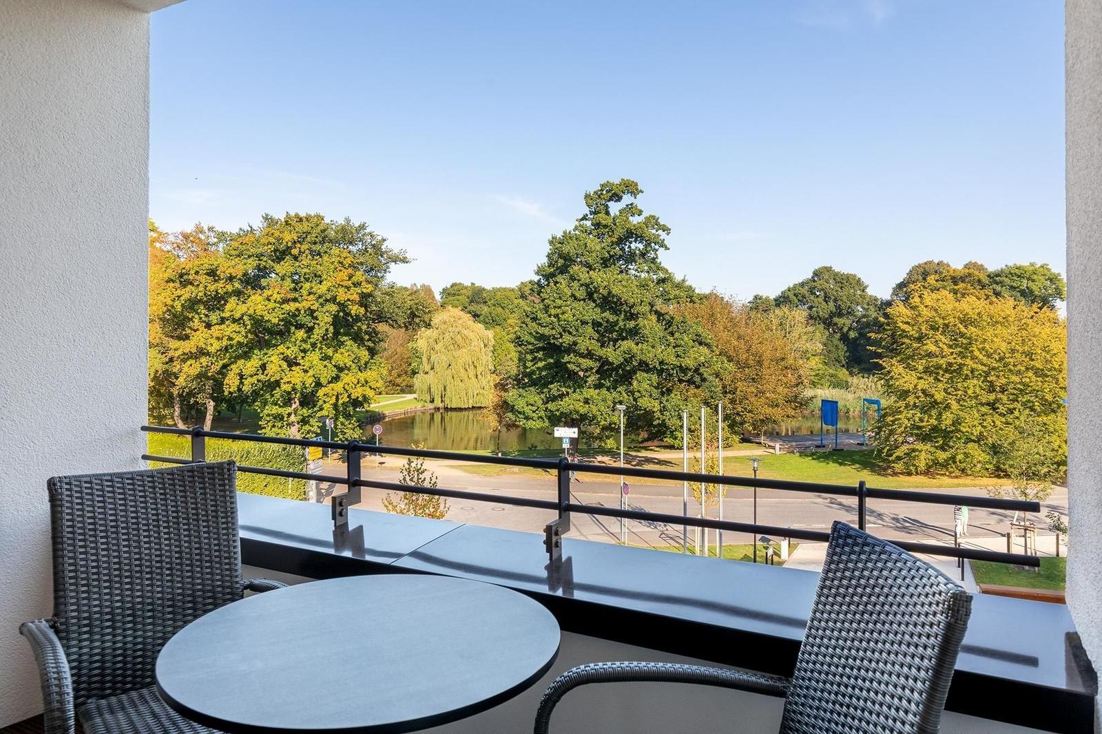 Terrasse mit Tisch und Stühlen, Blick auf einen See und Bäume.