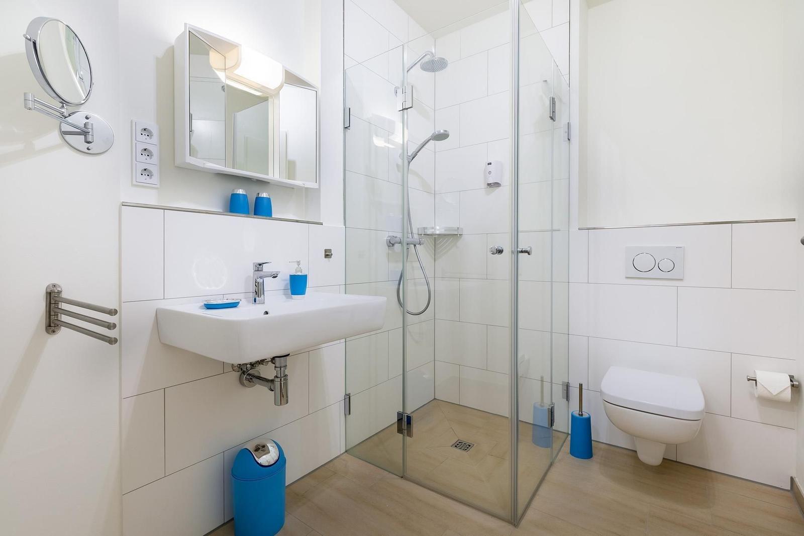 Badezimmer mit Dusche, Waschbecken und WC. Blaue Accessoires und weiße Fliesen.