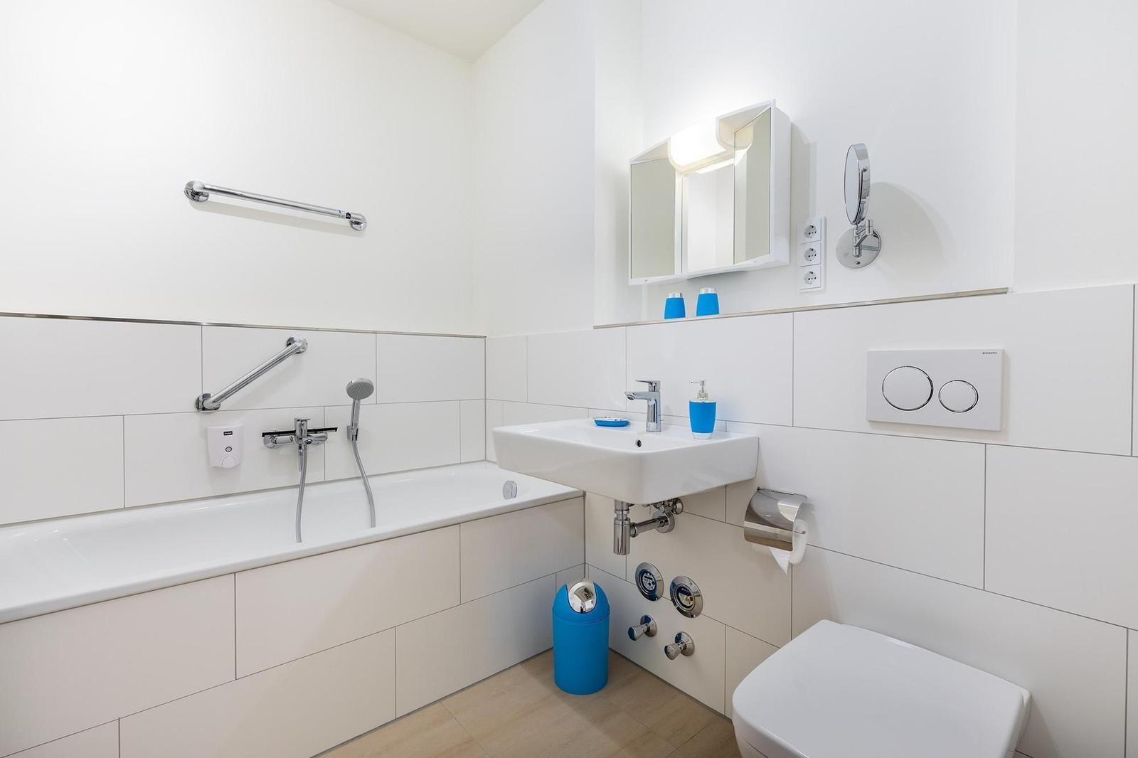 Badezimmer mit Badewanne, Waschbecken und Toilette. Blaue Accessoires und Handlauf.