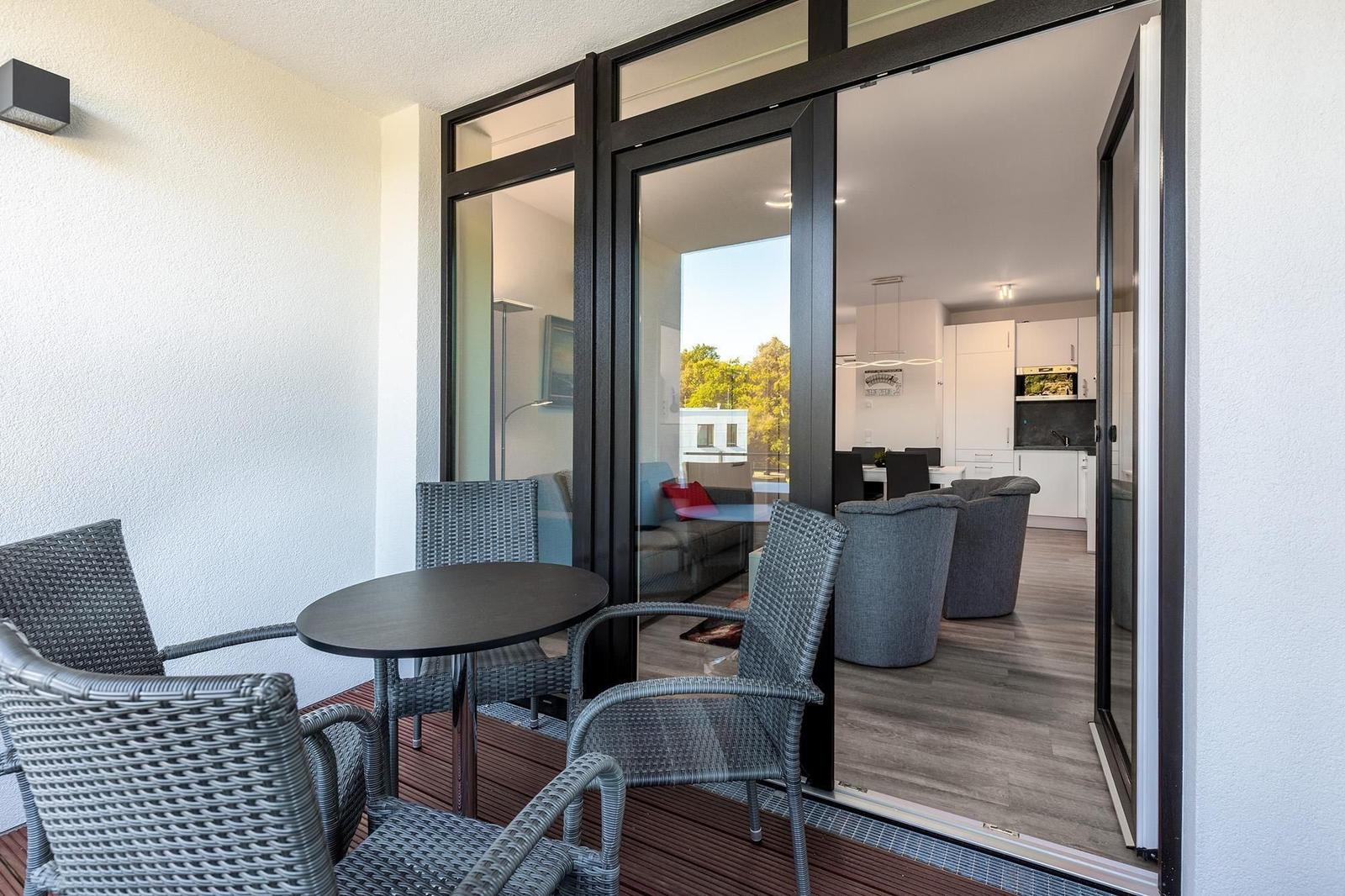 Terrasse mit Tisch und Stühlen. Durch Glastüren ist Wohn- und Küchenbereich sichtbar.