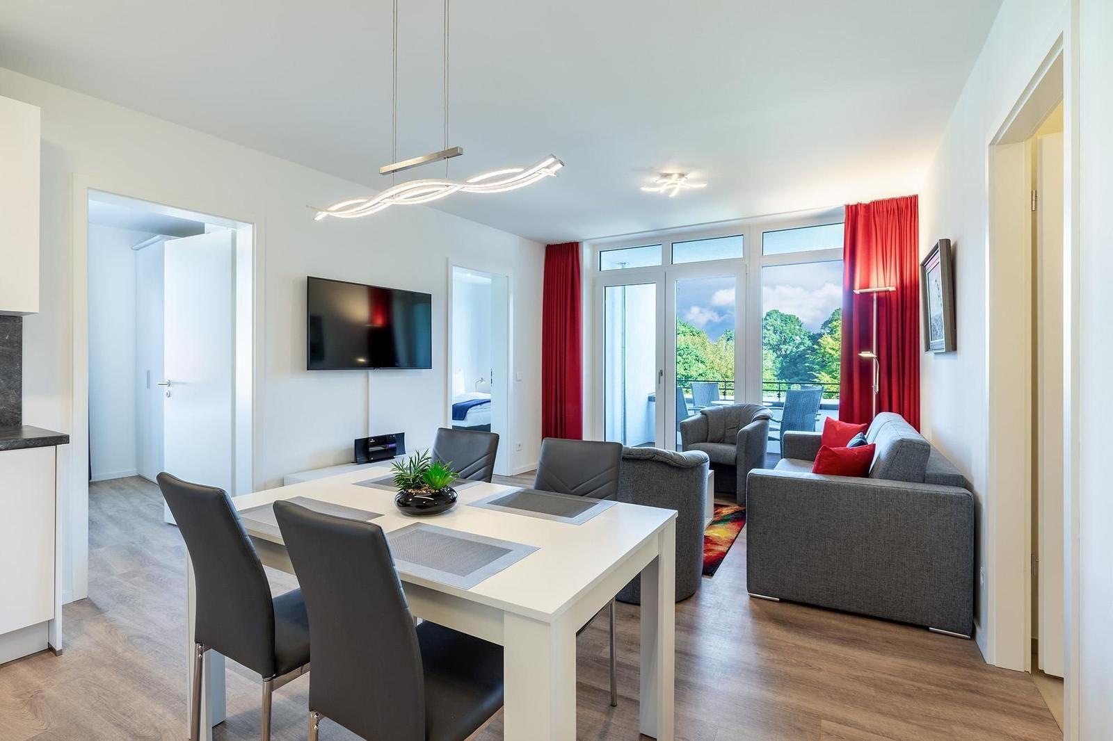 Wohn- und Essbereich mit TV, Esstisch und Balkonansicht.