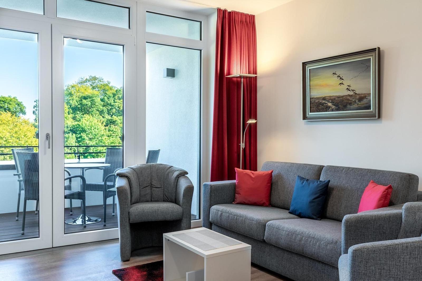 Wohnzimmer mit Sofa, Sessel und Balkon. Rote Vorhänge und Wandbild.
