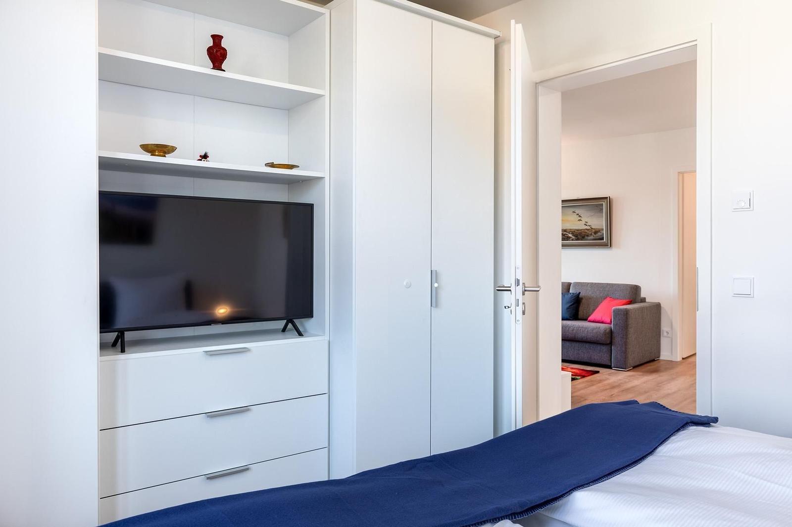 Schlafzimmer mit TV, Kleiderschrank und Blick in Wohnbereich.