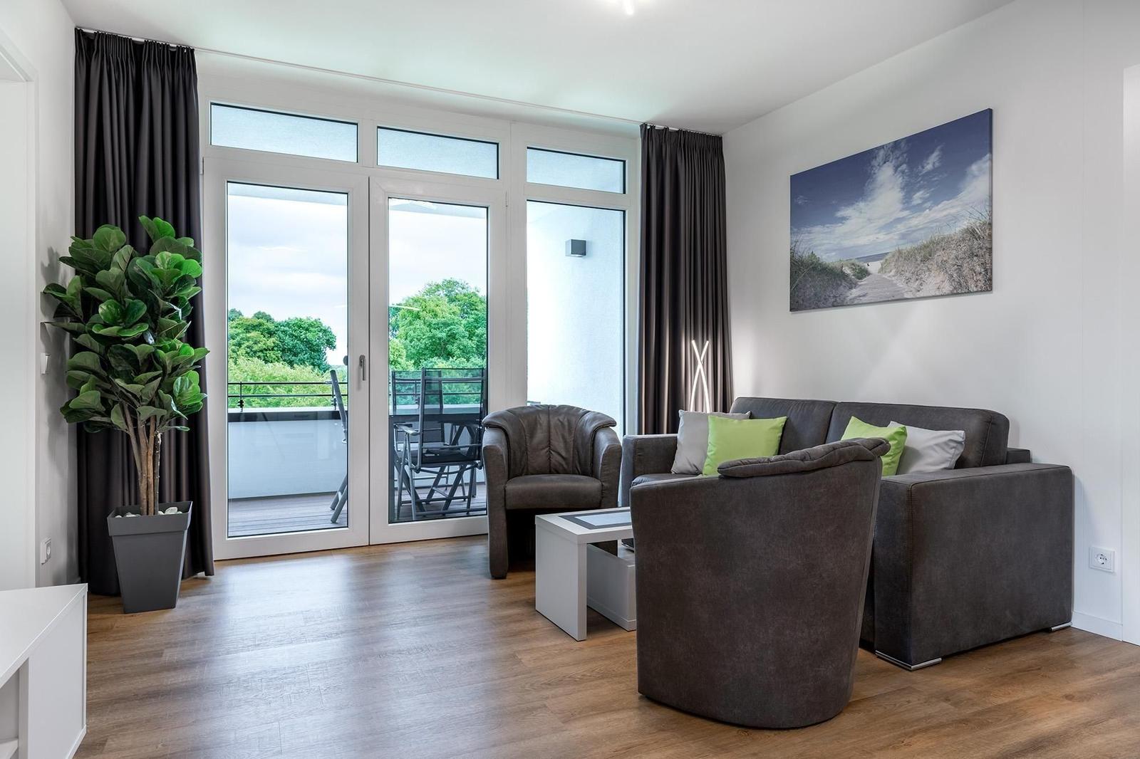 Wohnzimmer mit Sofa, Sessel und Balkonansicht.