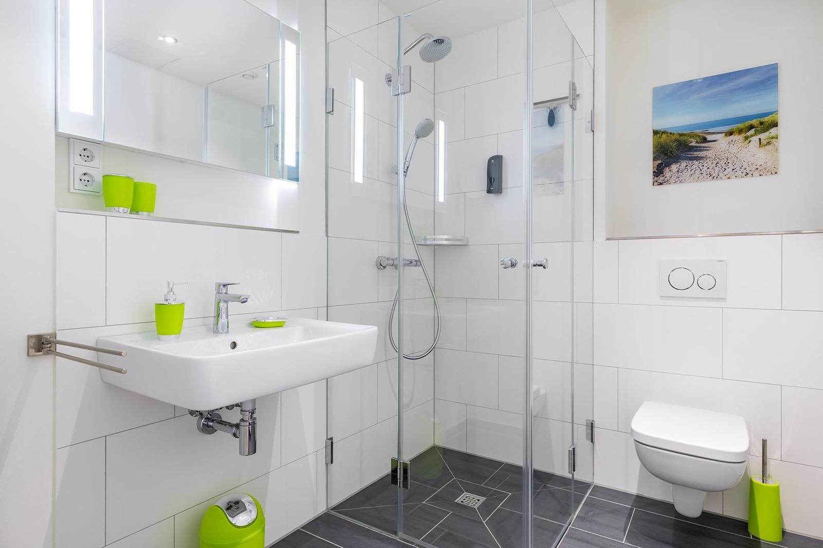 Badezimmer mit Dusche, Waschbecken und WC. Grüne Accessoires und Strandbild.