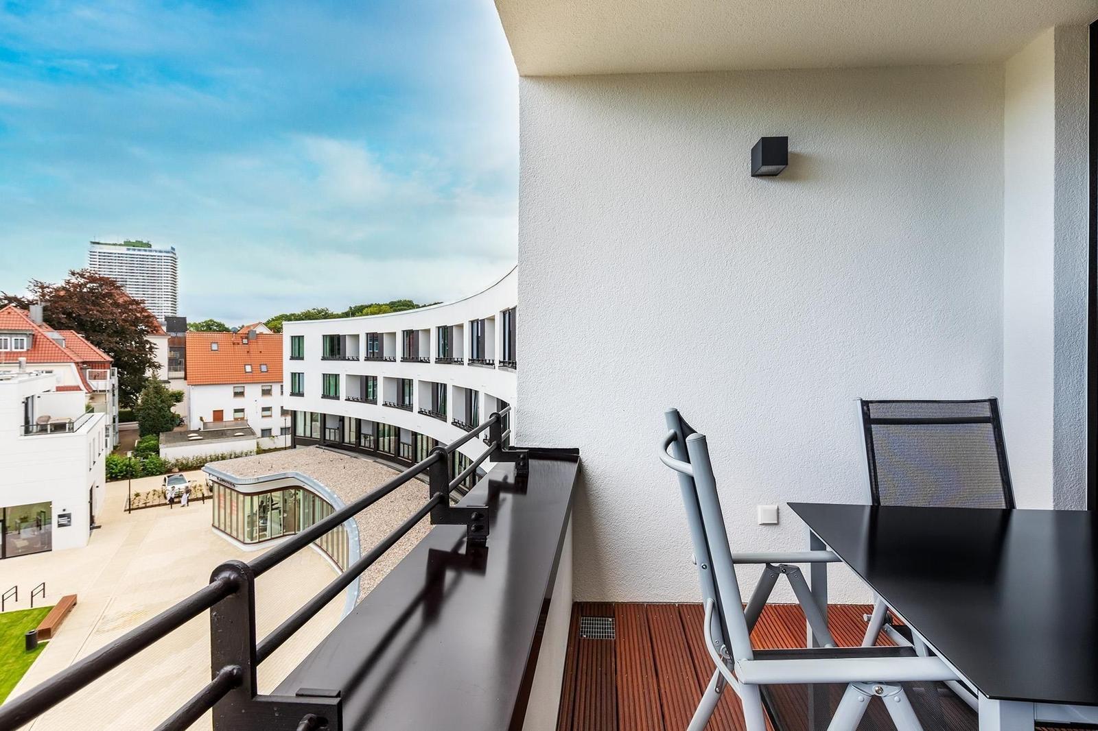 Terrasse mit Tisch und Stühlen. Blick auf moderne Gebäude und Park.