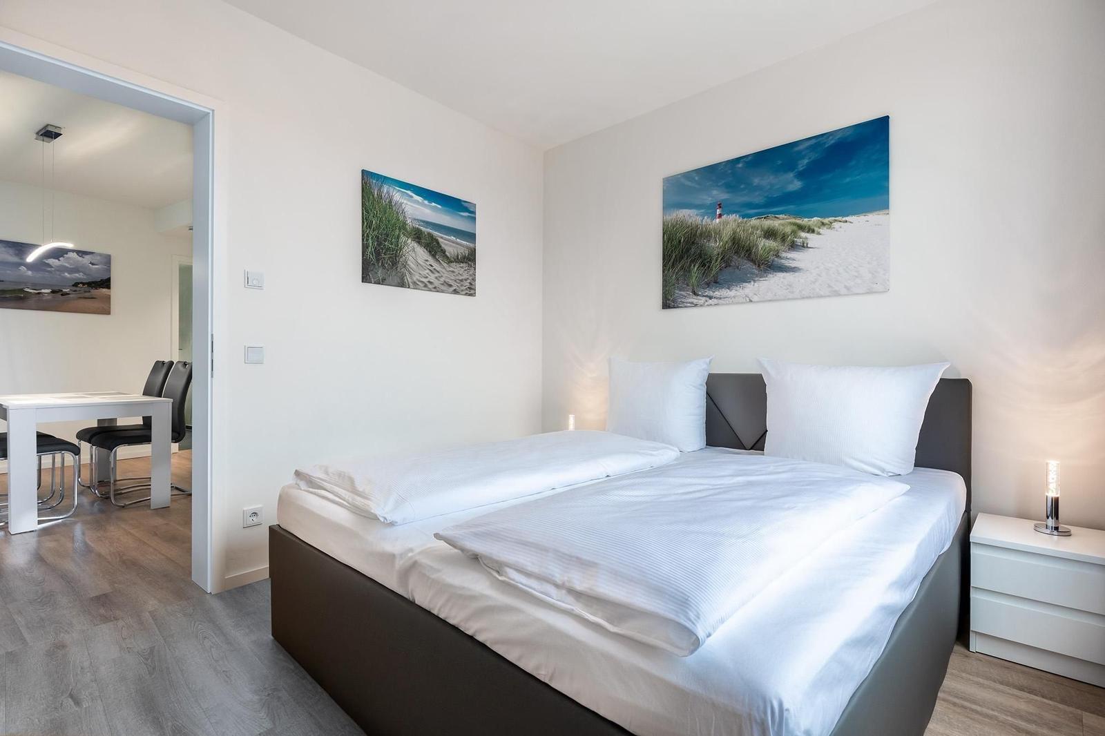 Schlafzimmer mit Doppelbett, Wandbildern und Sicht in die Küche.