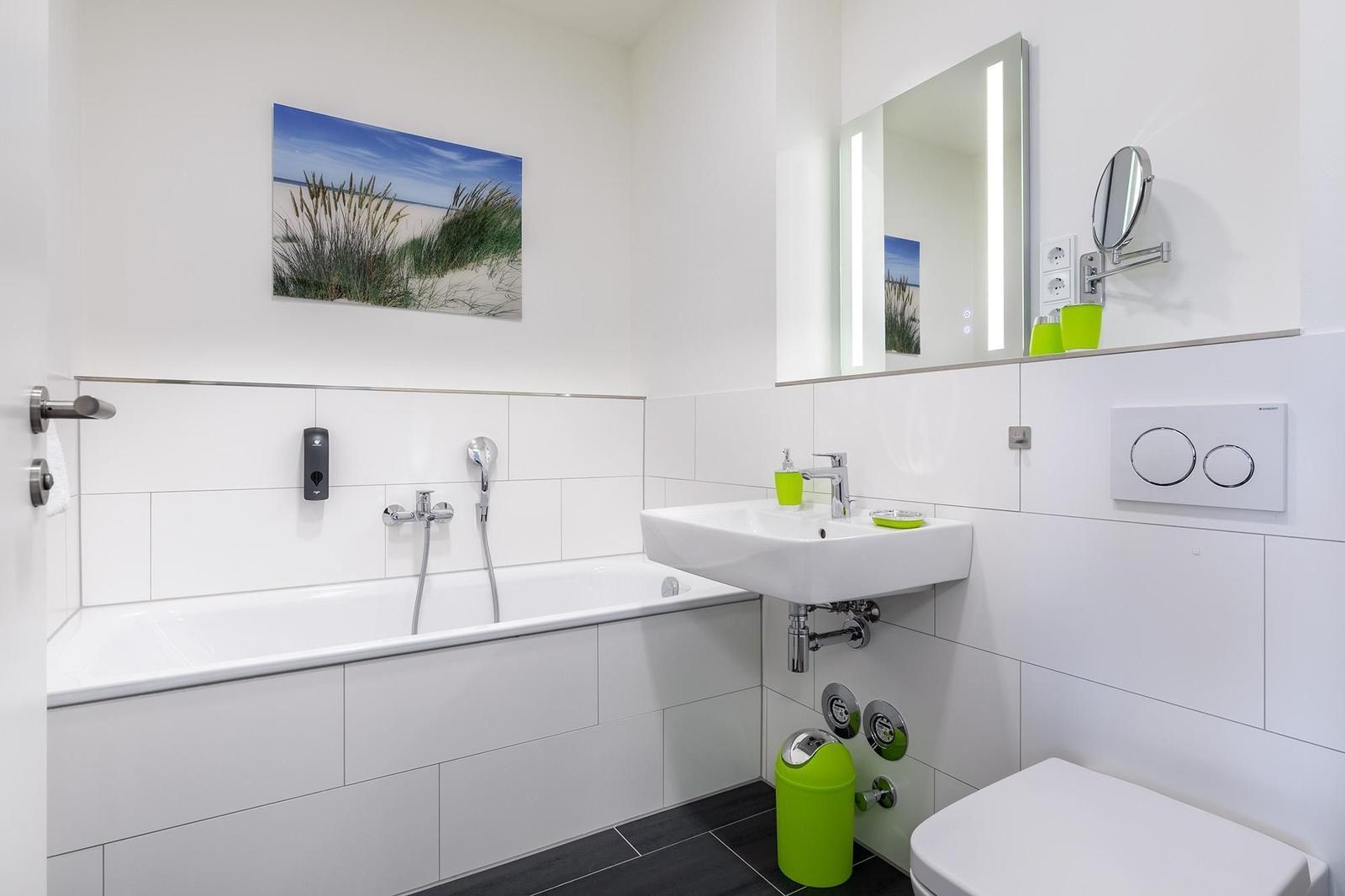 Badezimmer mit Badewanne, Waschbecken und Toilette. Grüne Accessoires und Spiegel.