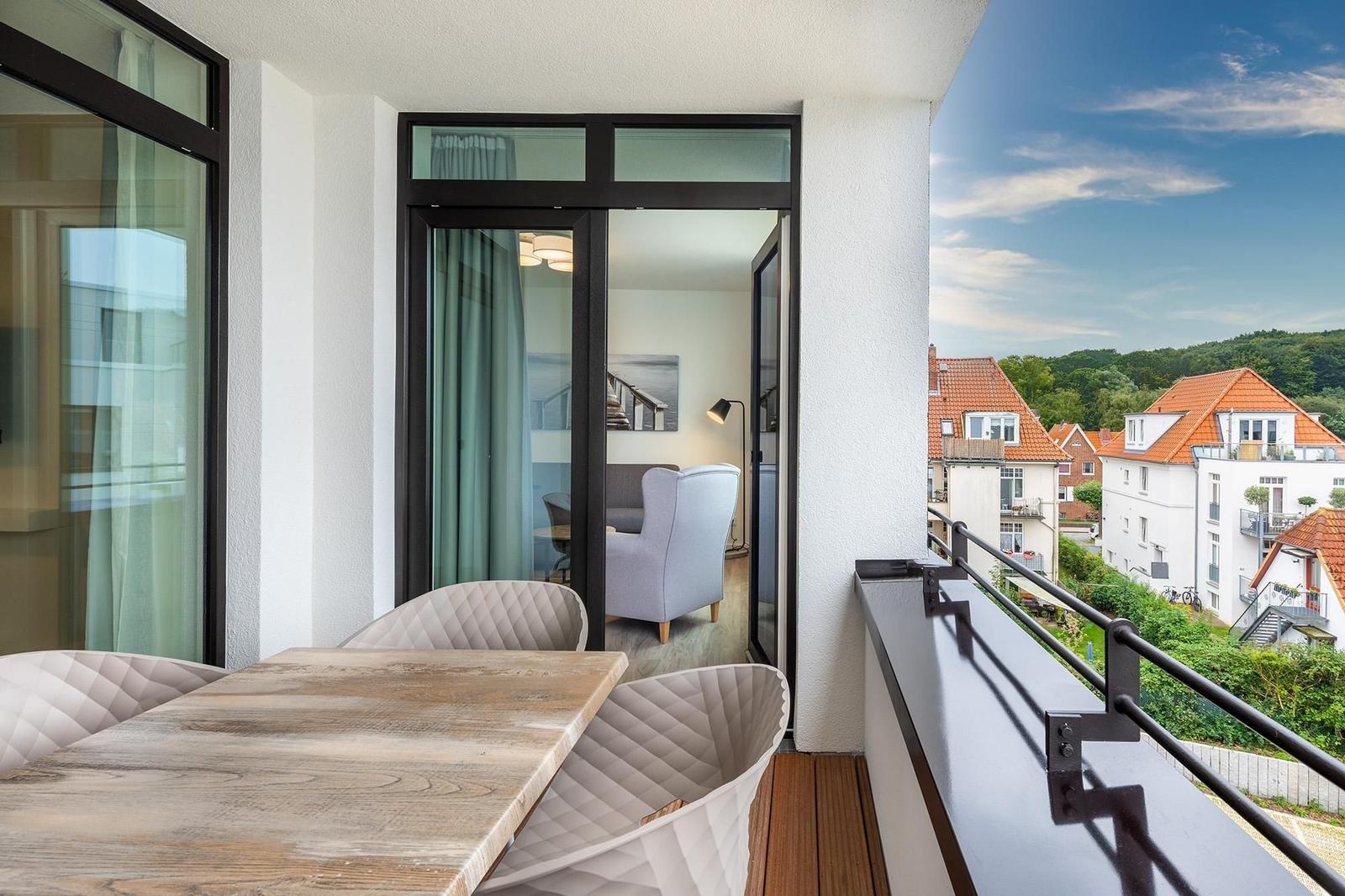Terrasse mit Tisch und Stühlen, Blick auf Dächer und Grün.
