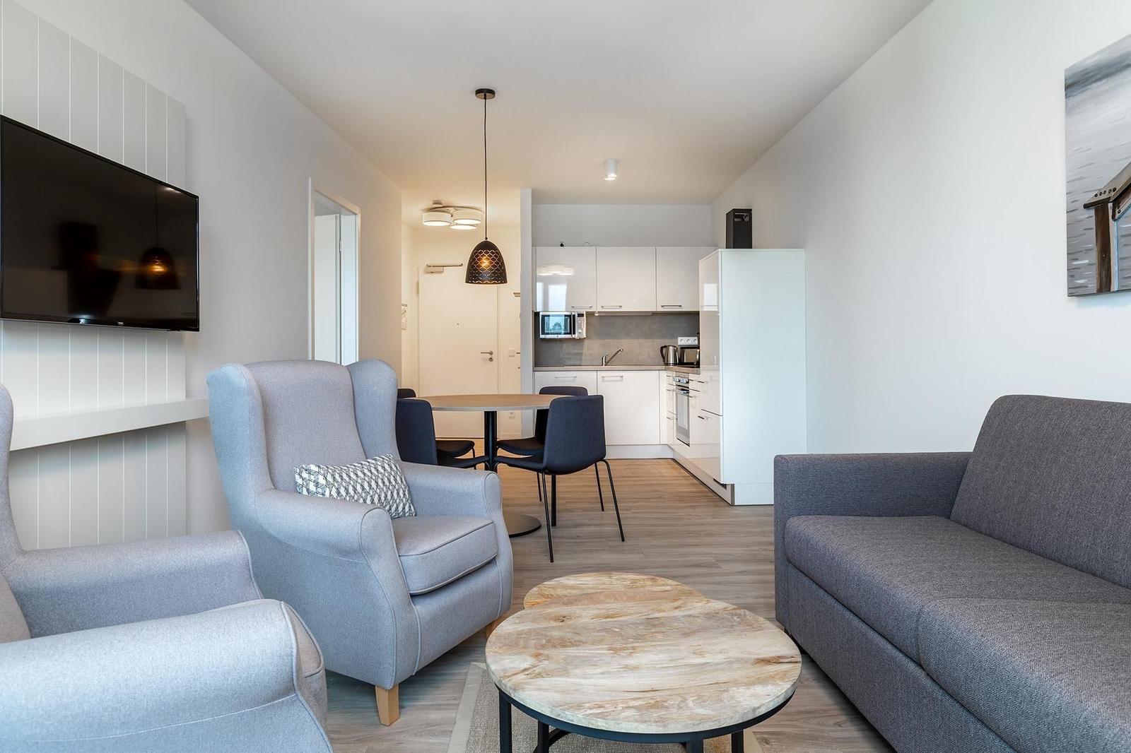 Wohnzimmer mit Sofa, Sessel und Küchenbereich im Hintergrund.