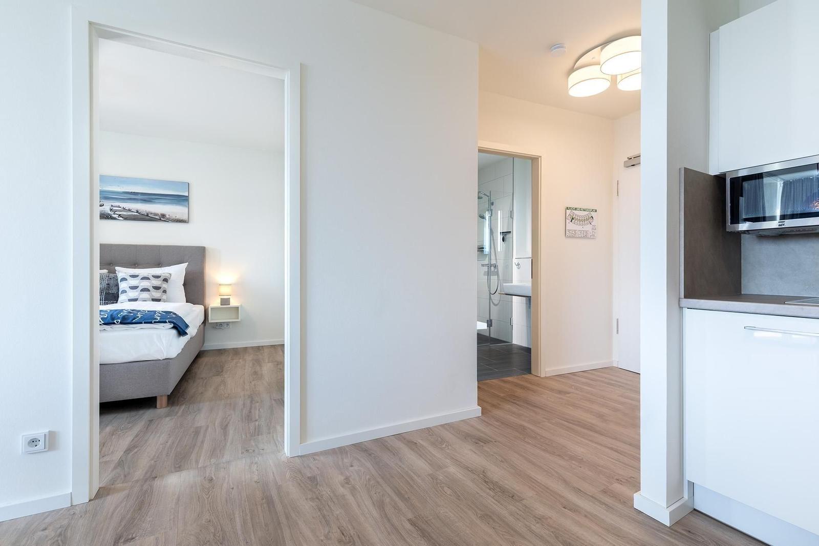 Schlafzimmer, Bad und Küche sind sichtbar. Holzdielen und weiße Wände.