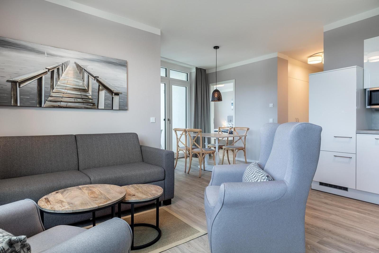 Wohn- und Essbereich mit Sofa, Sessel und Esstisch. Wandbild zeigt einen Steg.