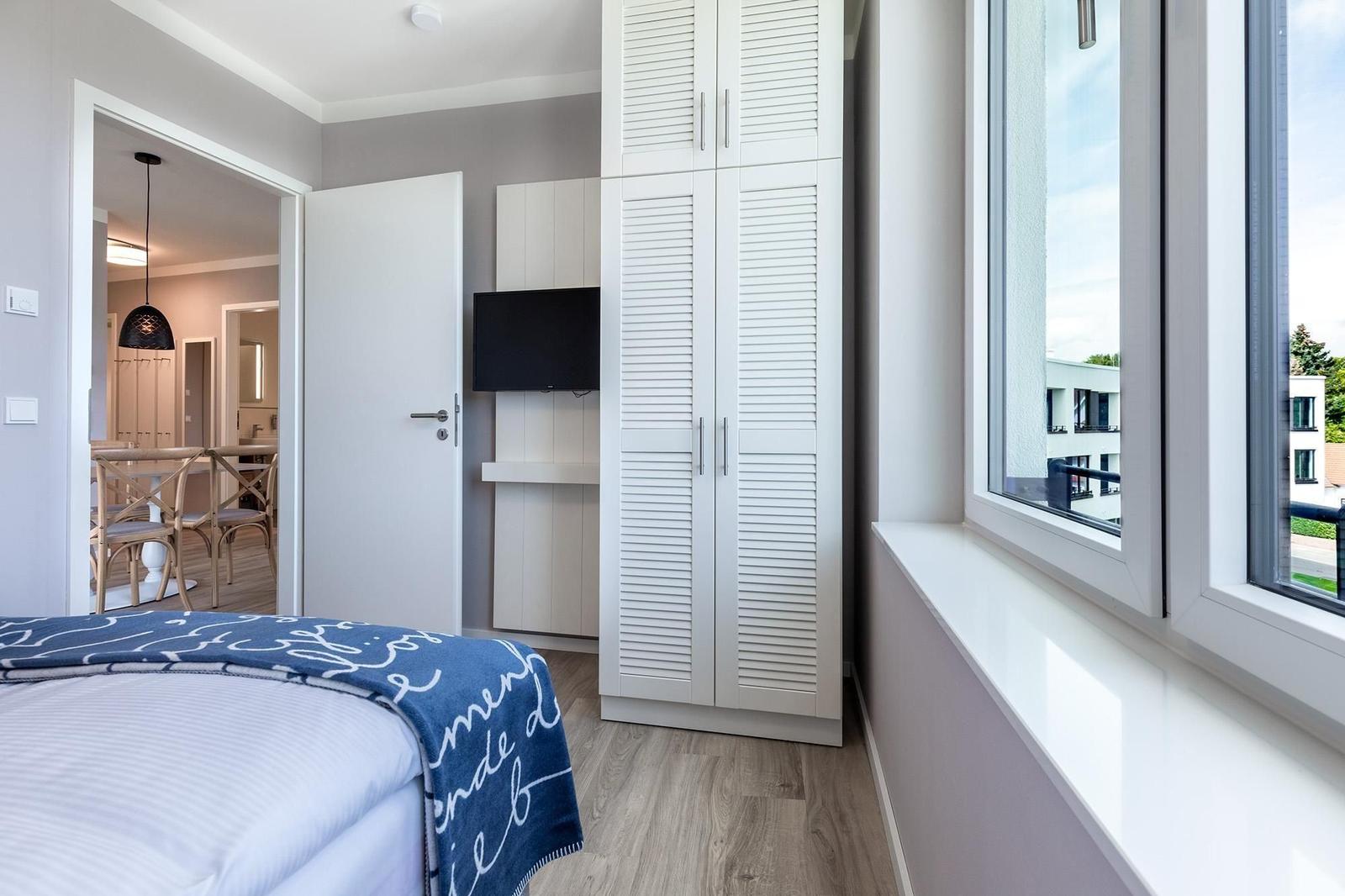 Schlafzimmer mit Bett, Kleiderschrank und Fenster. Durchgang zur Küche und Bad.