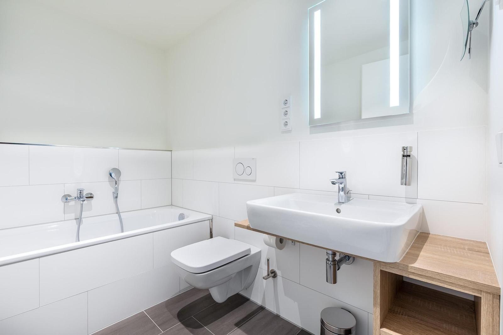 Badezimmer mit Badewanne, Toilette und Waschbecken mit beleuchtetem Spiegel.