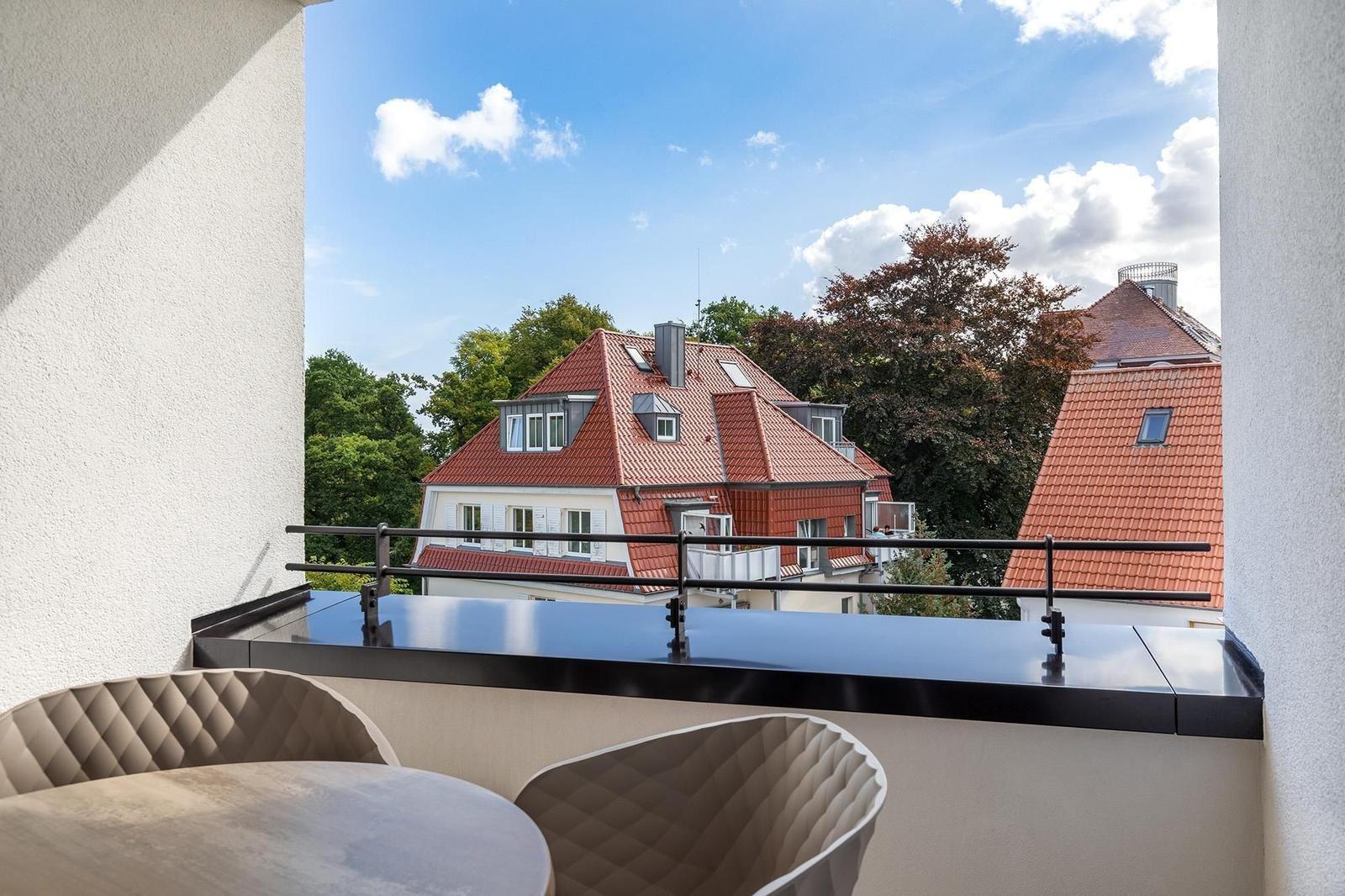 Terrasse mit Sitzgelegenheit und Blick auf rote Dächer und Bäume.