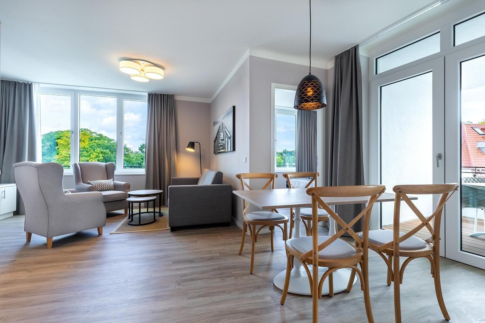 Wohn- und Essbereich mit Holzboden, Sitzgelegenheiten und Balkontür.