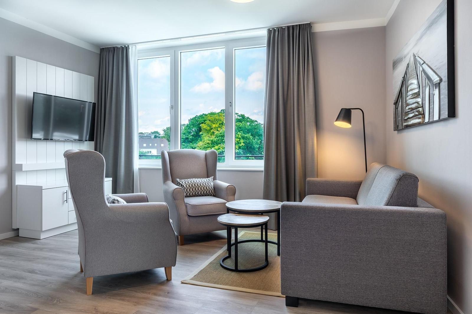 Wohnzimmer mit Sofa, zwei Sesseln und TV an der Wand.