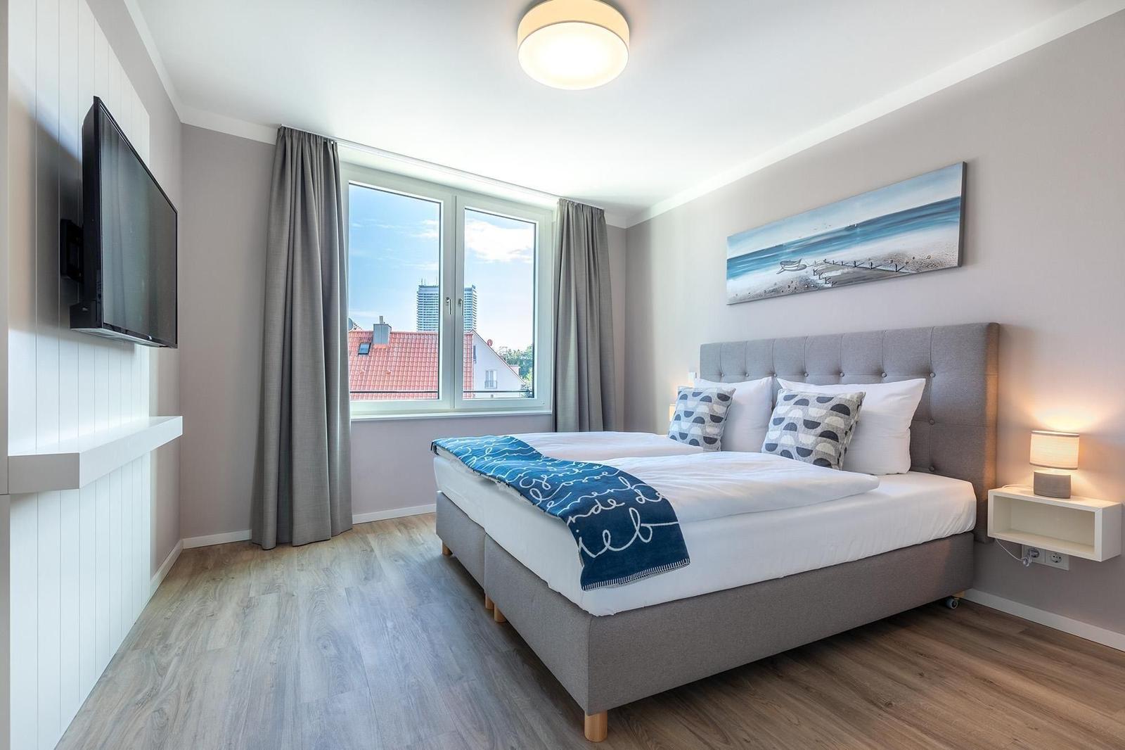 Schlafzimmer mit Doppelbett, Fenster und Wandbild.