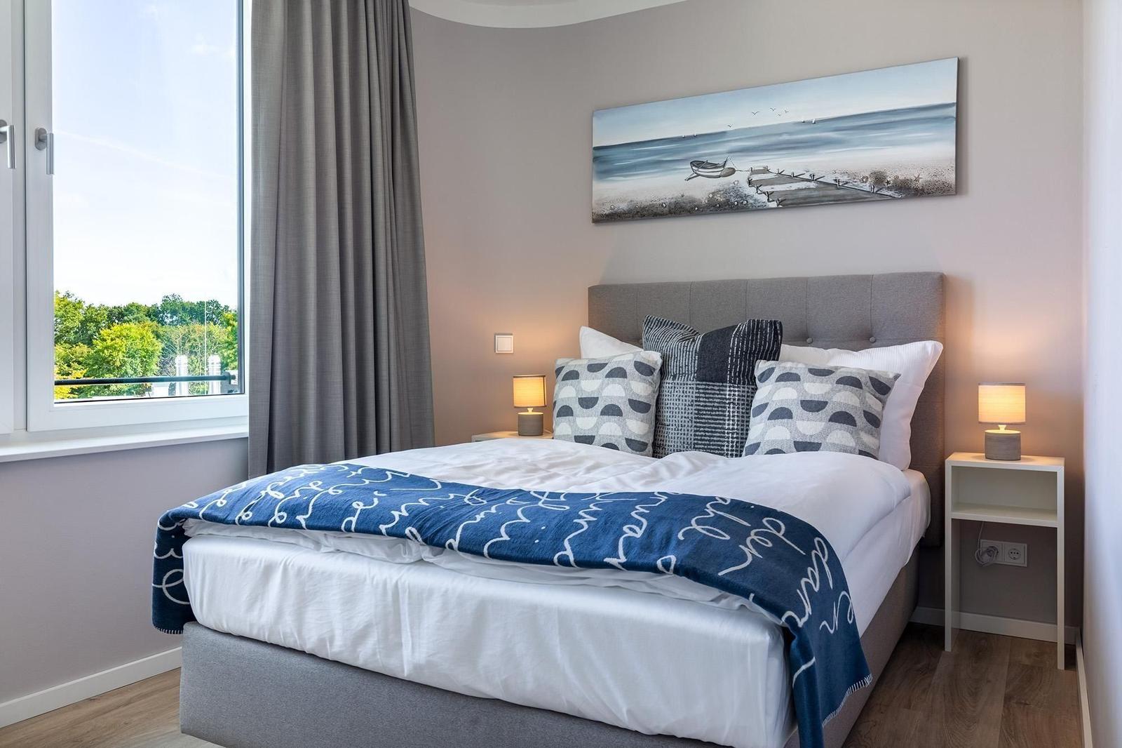 Schlafzimmer mit Bett, Nachttischen und Fensterblick auf Grün.