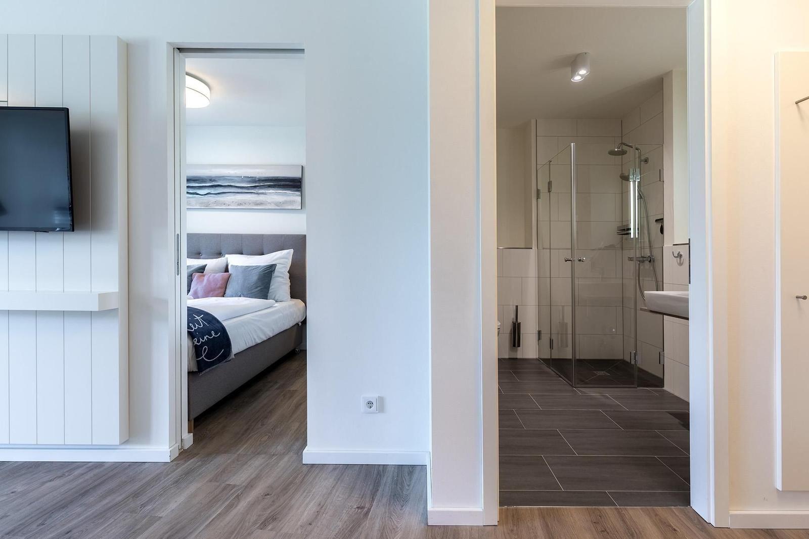 Schlafzimmer mit Bett und Bad mit Dusche und Waschbecken