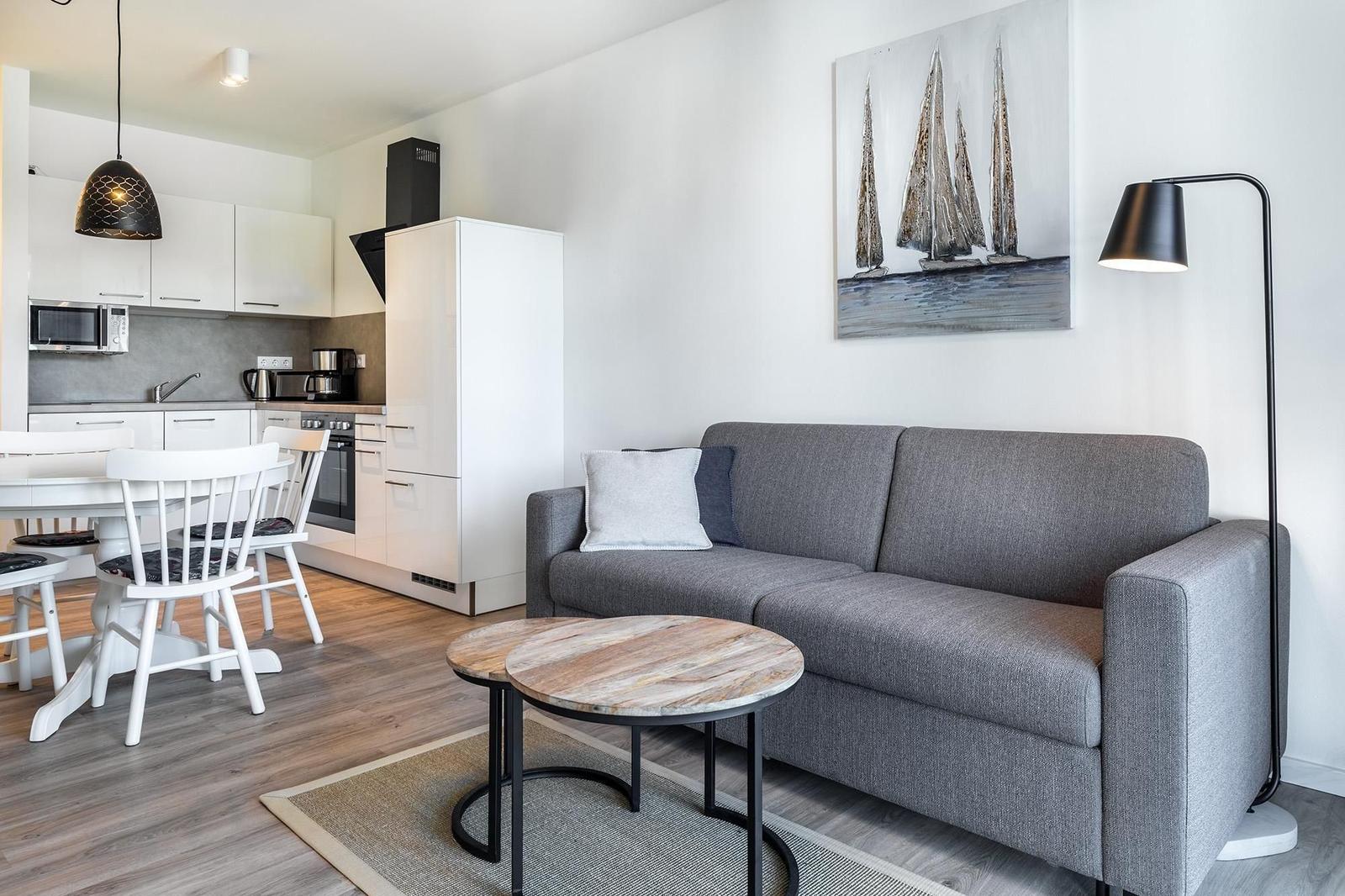 Wohnzimmer mit Sofa, Tisch und Küchenbereich im Hintergrund.