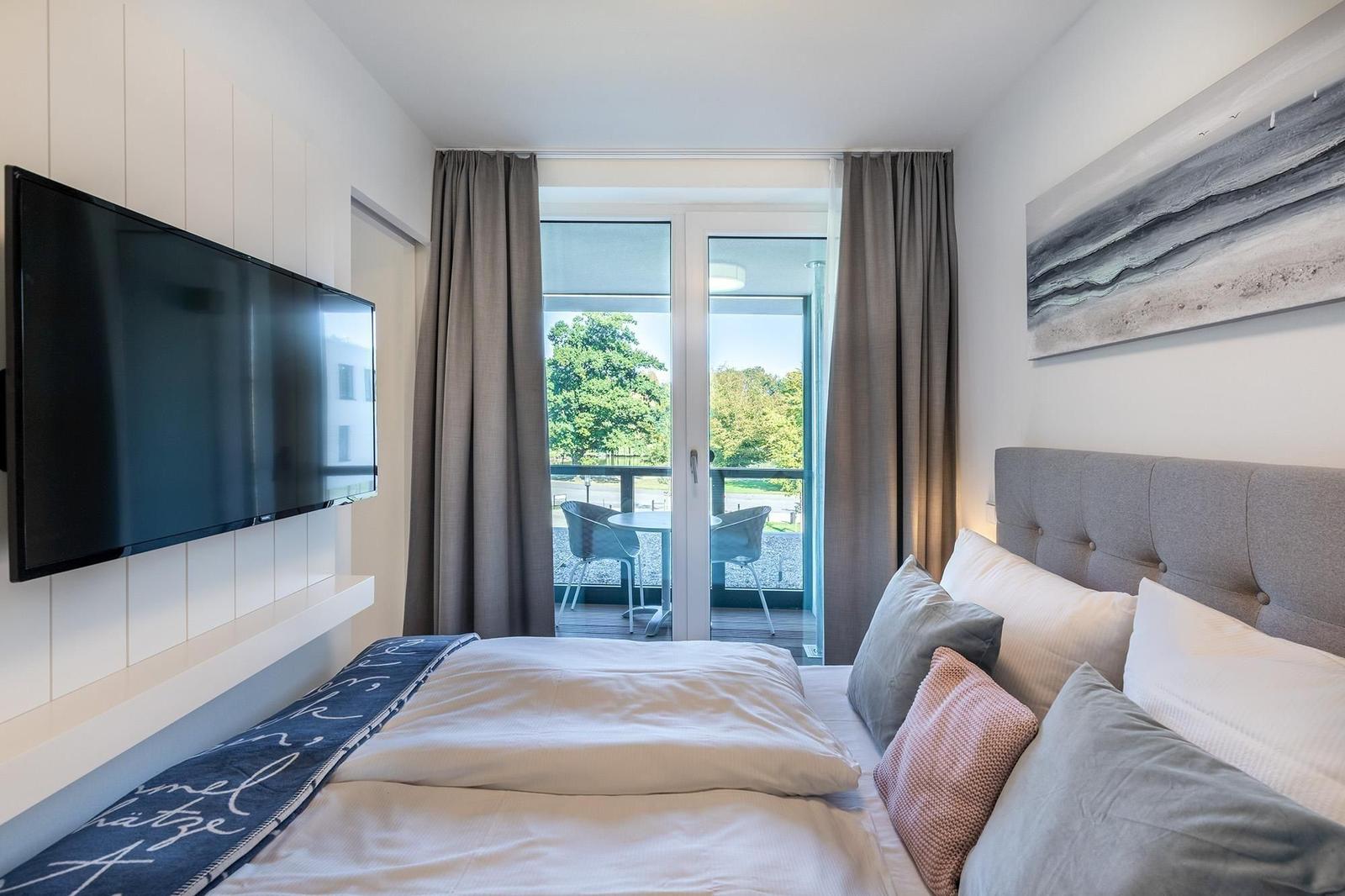 Schlafzimmer mit Bett, TV und Balkon mit Tisch und Stühlen.