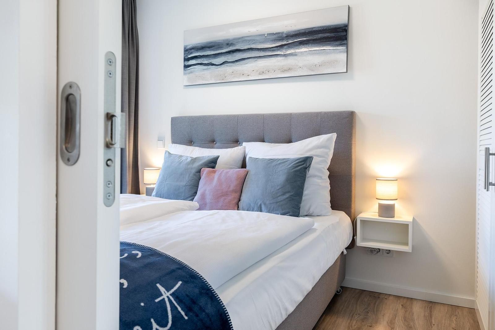 Schlafzimmer mit Bett, Kissen und Wandbild.