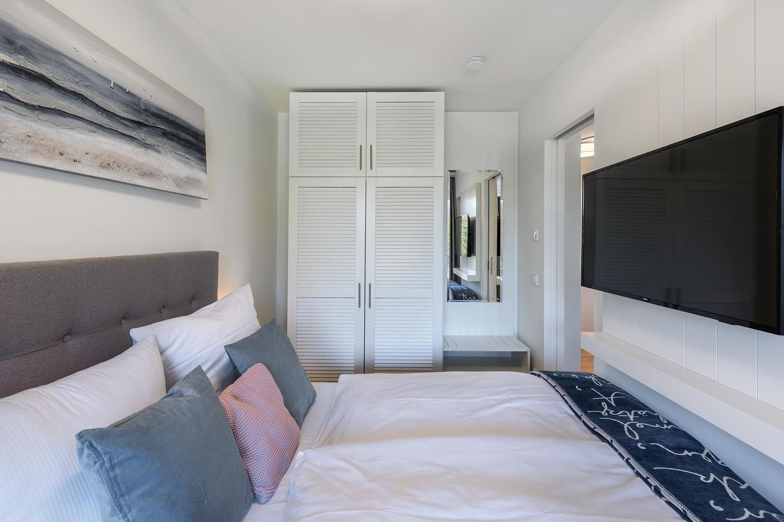 Schlafzimmer mit Bett, Kleiderschrank und Fernseher an der Wand.